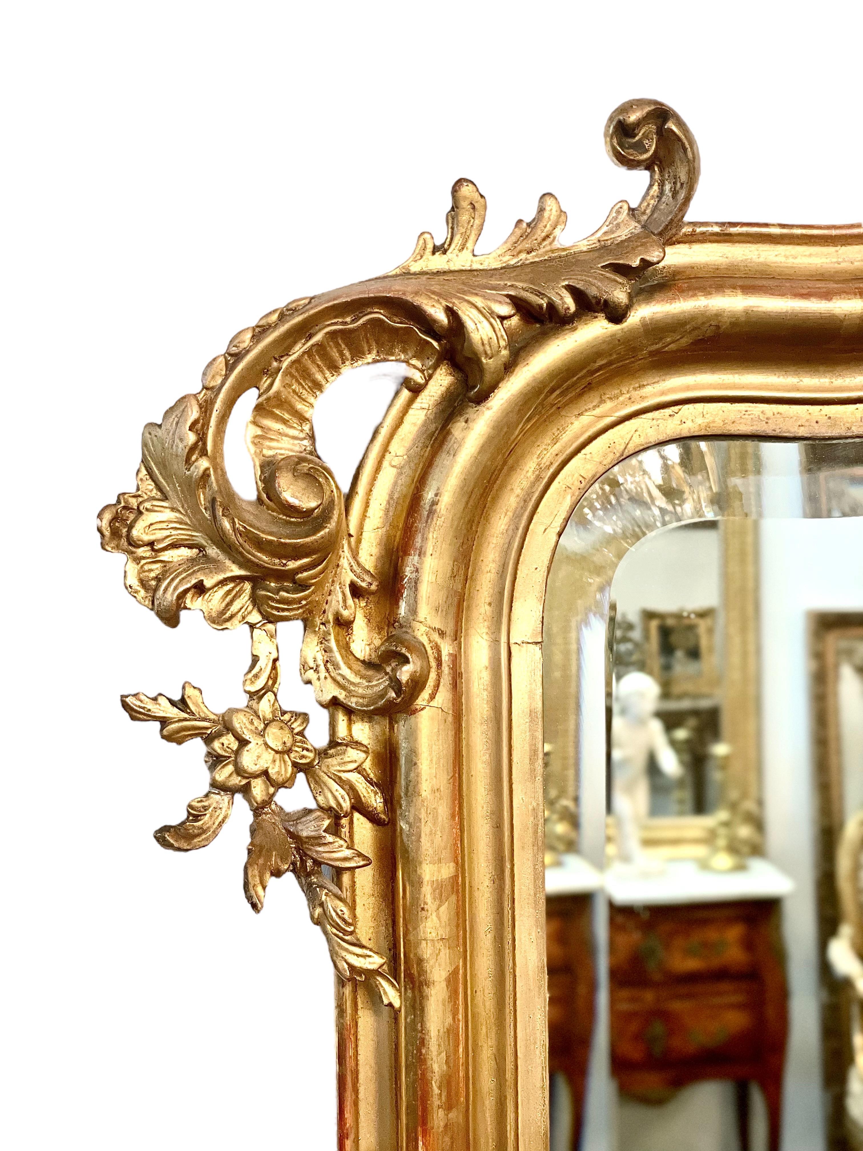 Ein absolut atemberaubender vergoldeter und geschnitzter Holzspiegel im Louis XV-Stil aus der zweiten Hälfte des 19. Jahrhunderts mit einem übergroßen Kokardenwappen, flankiert von phantasievollen Blättern und Blumen. Zusätzliche Verzierungen an den