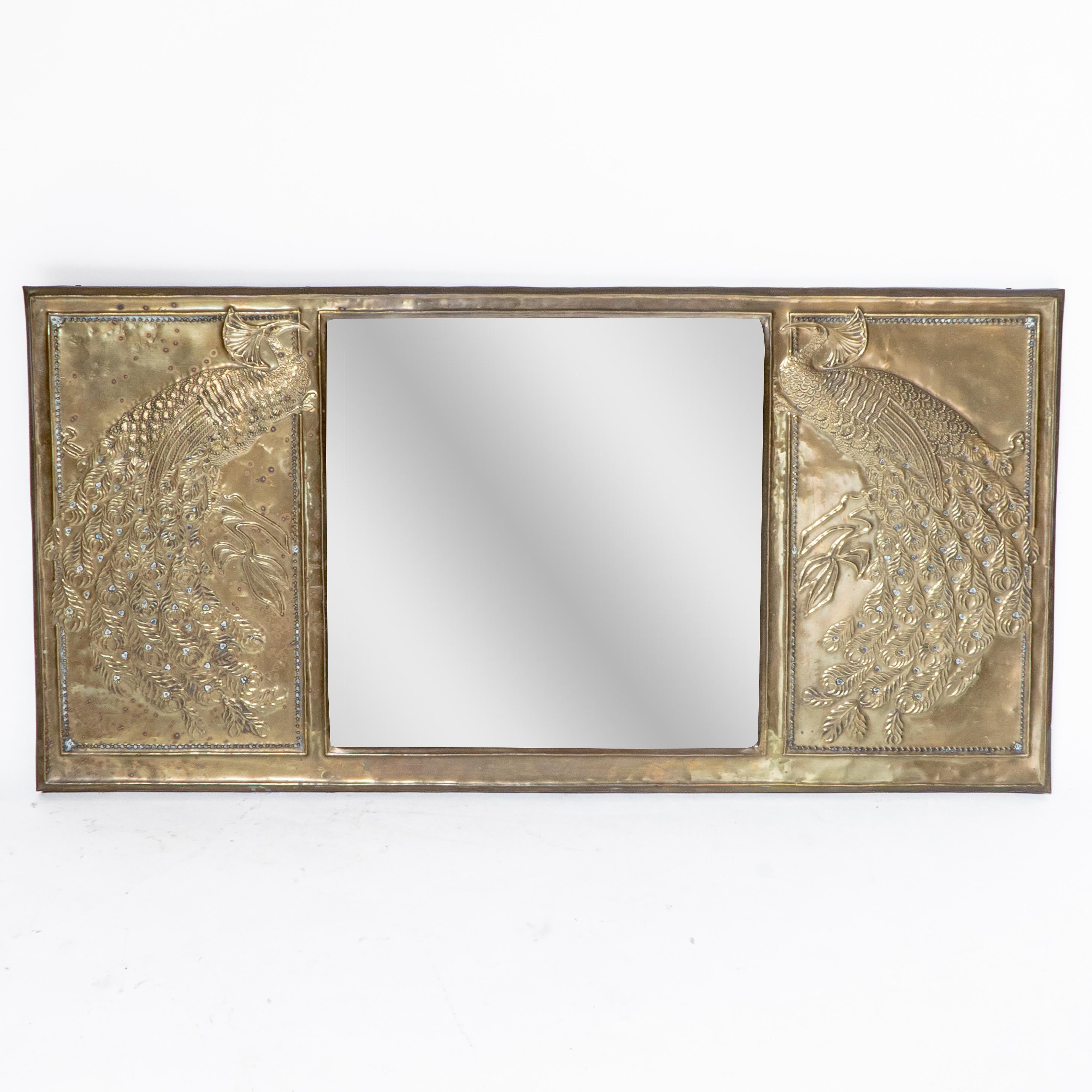 An Aesthetic Movement brass mirror with stylized Peacocks perched on a branch decorated to each side and retaining the original bevelled mirror.