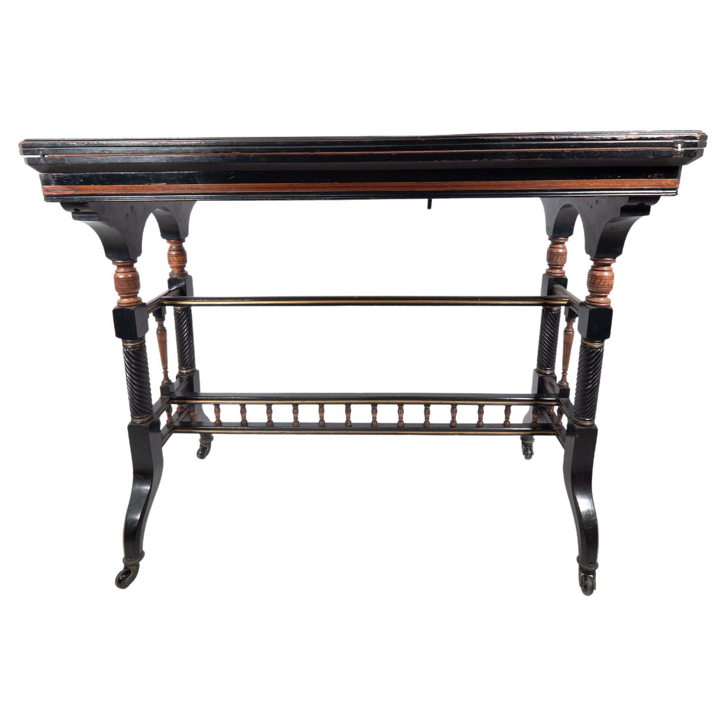 Gillows attributed. An Aesthetic Movement ebonized fold over and swivel top card table with the original red baize to the playing area. The rectangular top when closed and the upper sides have inlaid floral decoration, with incised boxwood turnings