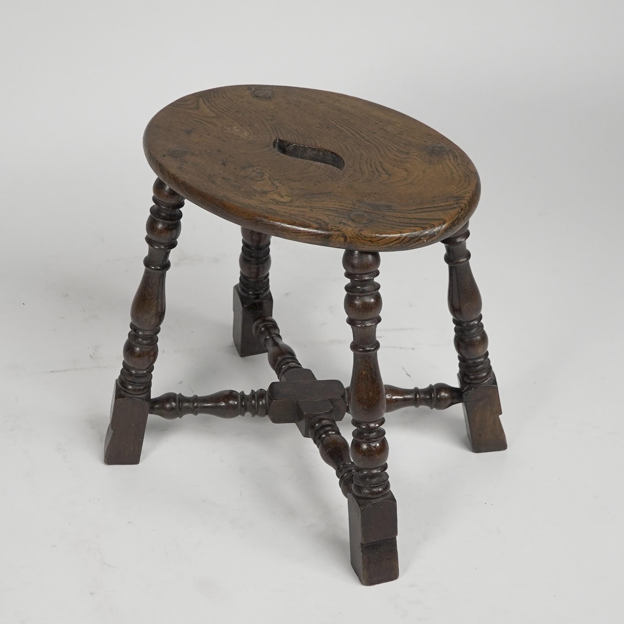 An Aesthetic Movement period Elm stool with a 'S' shaped pierced handle, and a wonderful wild grain to the seat. Tight through and exposed joints to the four corners of the seat with tiny little wedges hammered into those exposed circular tops. The