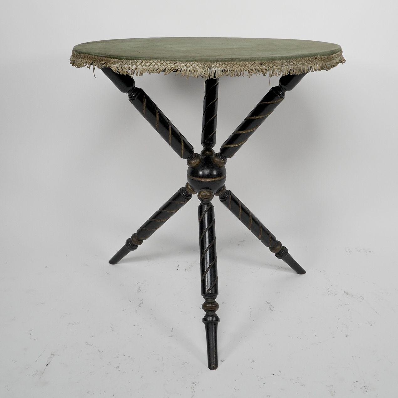 An Aesthetic Movement ebonized and gilded 'Gypsy' side table, with a circular top, retaining the original green baize top and shallow tassels below. The three upright supports and the three legs meet to a central ball in the middle.