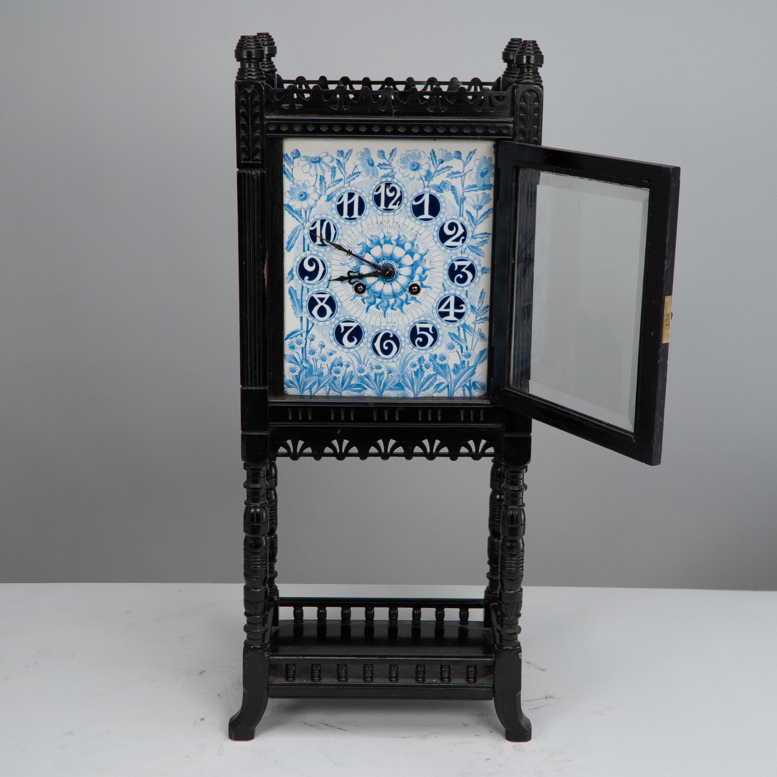 Lewis Foreman Day for Howell James & Co. An Aesthetic Movement mantel clock with hand painted floral decoration and sunflower to the dial flanked by tramway details with fretted decorations on turned supports with a lower shelf and turned gallery on