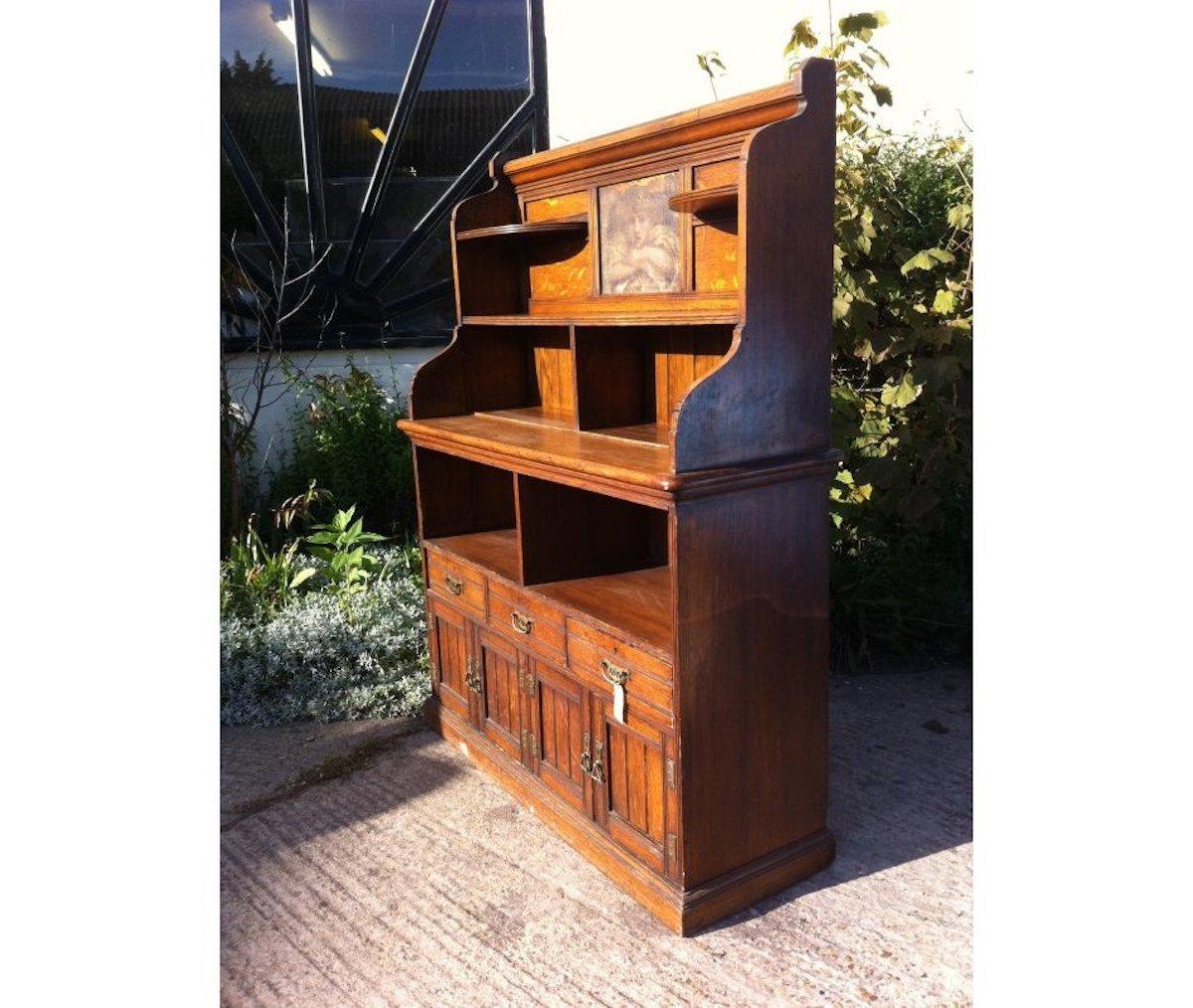 A good aesthetic movement oak bookcase or sideboard with a wonderful period oil painting on canvas to the top depicting a Pre-Raphaelite head and arms of a child in the style of Dante Gabriel Rossetti, flanked by semi-circular shelves and an open