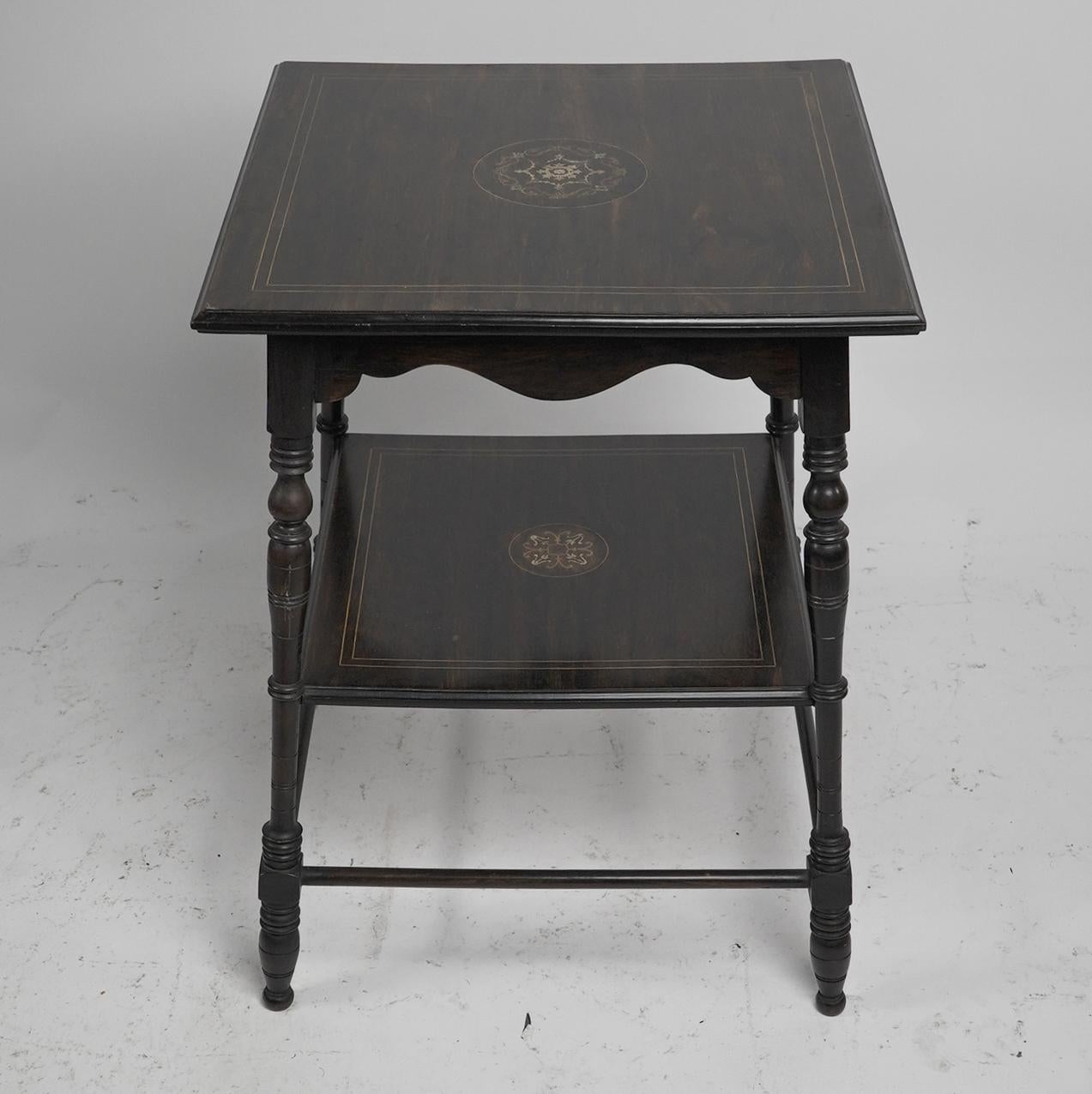 An Aesthetic Movement Rosewood two tier side table inlaid with floral decoration to the centres and parallel line inlay to edges of top and bottom shelf, stood on turned legs united by lower stretchers.