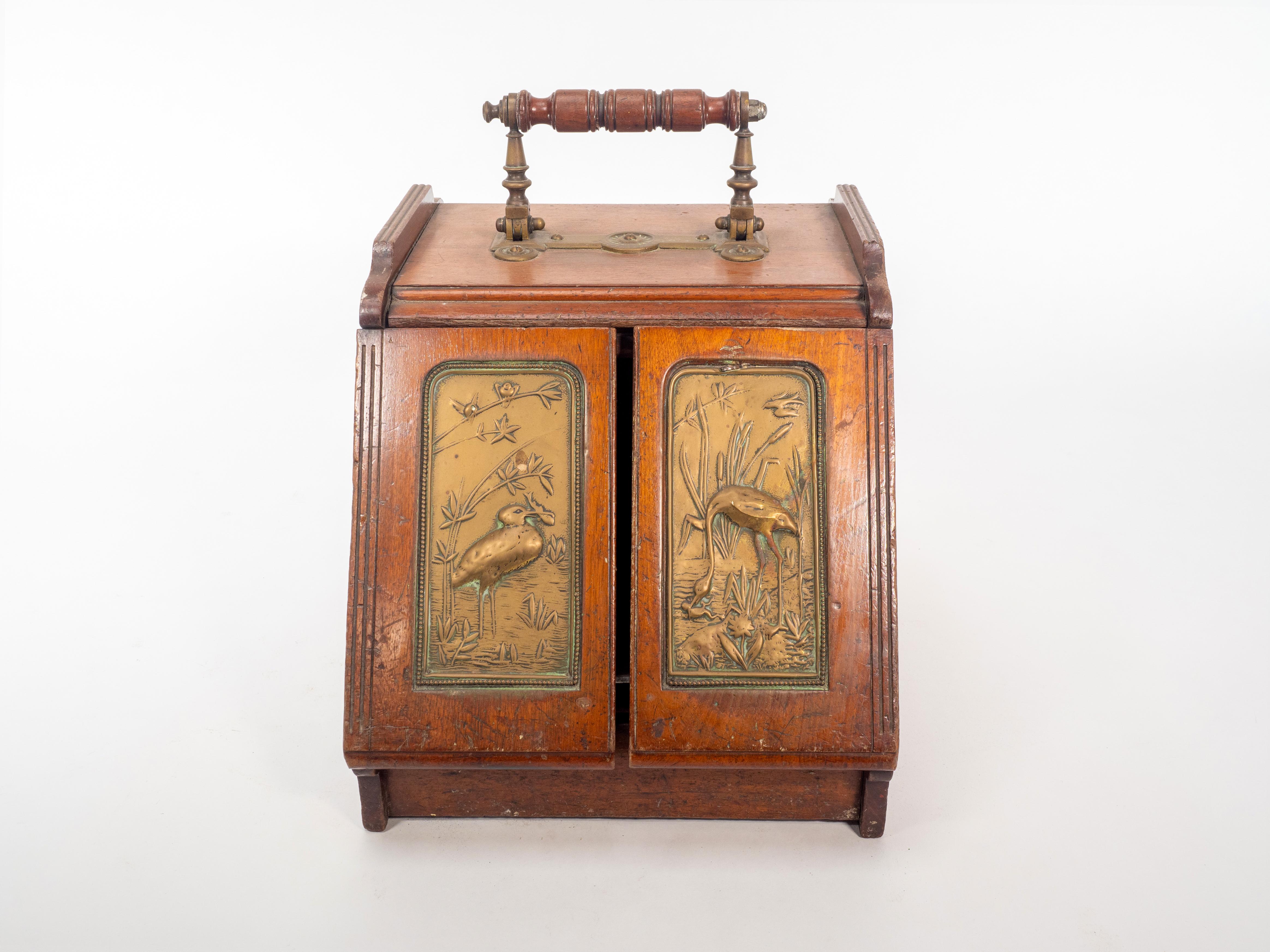 An Aesthetic Movement Walnut metamorphic oak coalbox. The handle when pulled back mechanically opens the two doors to the front, which has brass panels depicting Herons eating fish in a river scene with bullrushes and birds above them. The original
