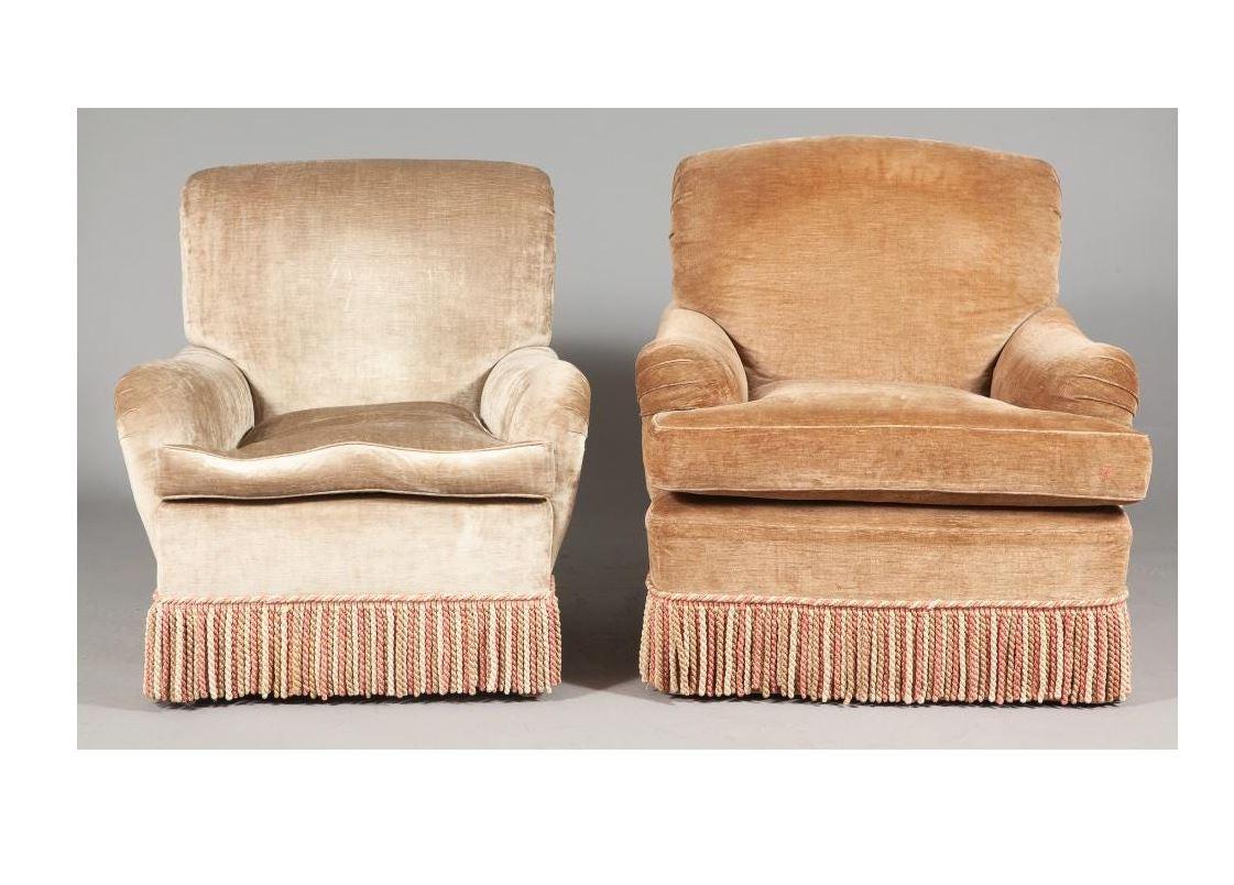 An almost pair of linen velvet swivel club chairs in brown and sand with bullion fringe.