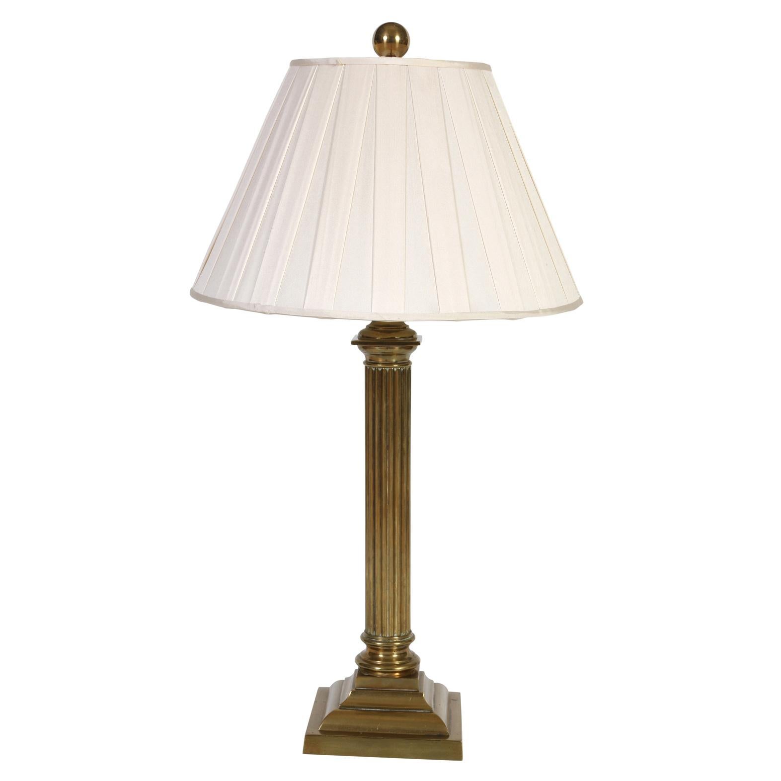 An almost pair of vintage brass column lamps and pleated ivory shades.  One lamp features a doric column and the other is a corinthian column.  Both brass lamps have a ribbed column with a square stacked base.  A classical pair of lamps add polish