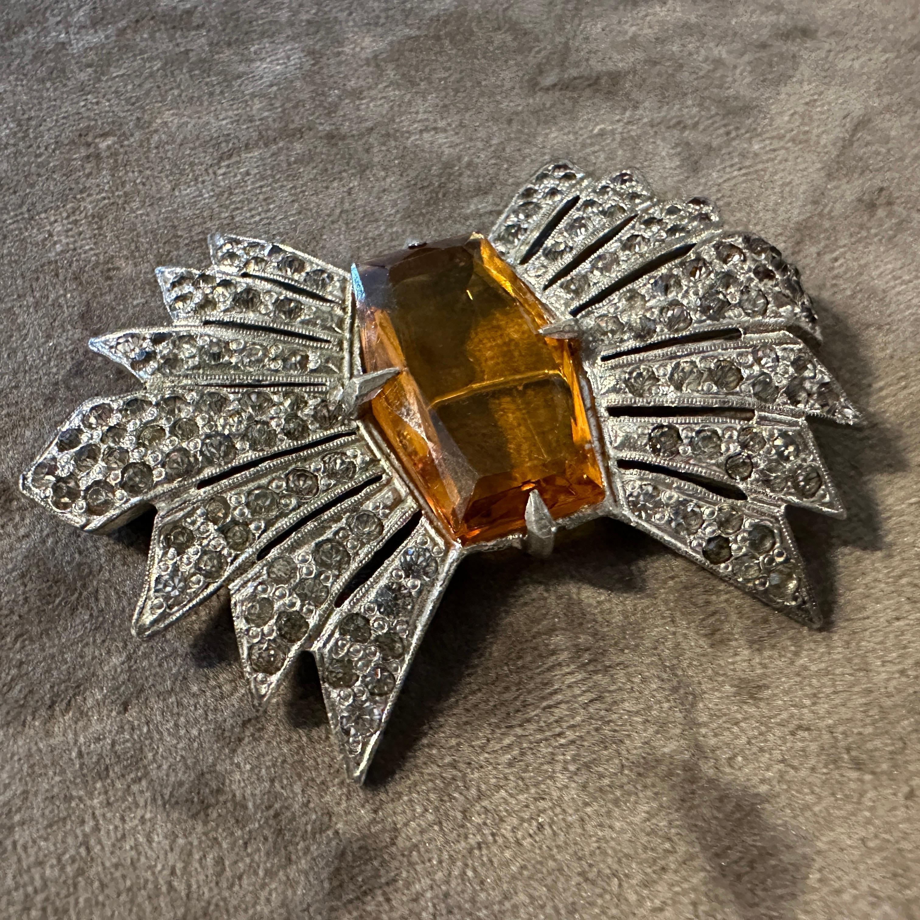 Erstaunlich 1930er Art Deco Modeschmuck Brosche
Versetzen Sie sich in den Glamour des Jazz-Zeitalters mit dieser schillernden Art-Déco-Brosche aus den 1930er Jahren. Die Brosche in Form eines kühnen Starburst-Motivs zeigt in der Mitte einen