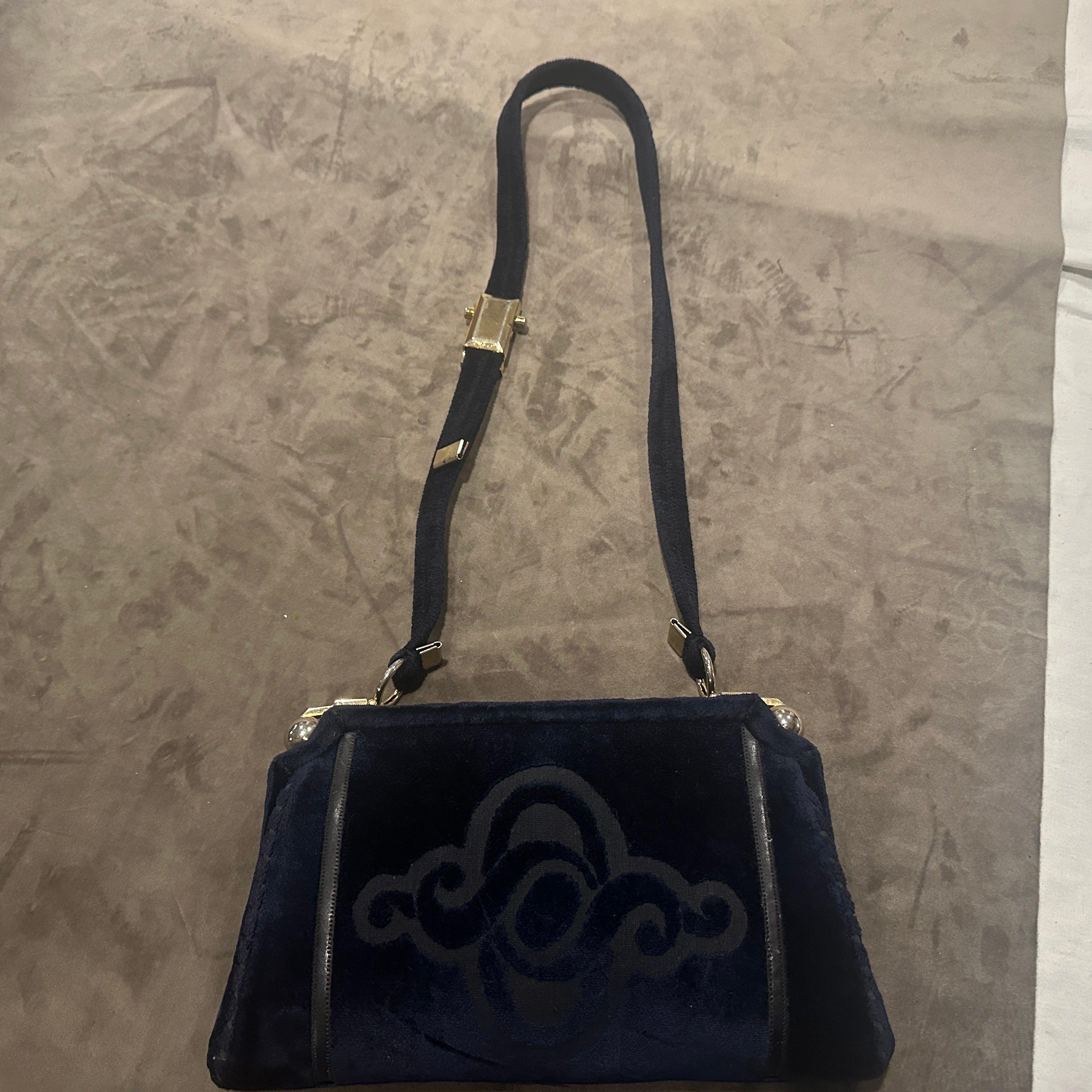 Fai un salto negli anni '80 con questa straordinaria borsa a tracolla italiana, realizzata in ricco velluto blu notte che trasuda lusso vintage. La borsa presenta una silhouette strutturata e trapezoidale che cattura perfettamente l'audace eleganza