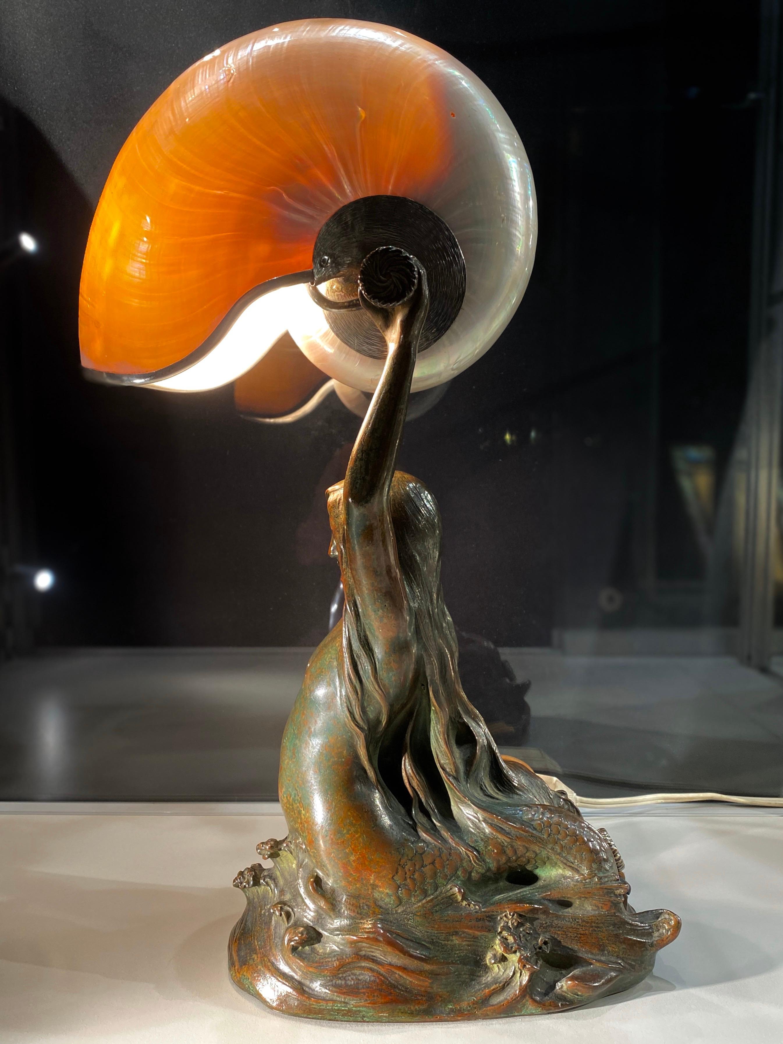 An extremely fine and very rare American Art Nouveau patinated bronze Tiffany Studios “Nautilus” desk lamp designed by, Louis Gudebrod and produced exclusively by Tiffany studios of depicting a beached mermaid holding breaking through the waters