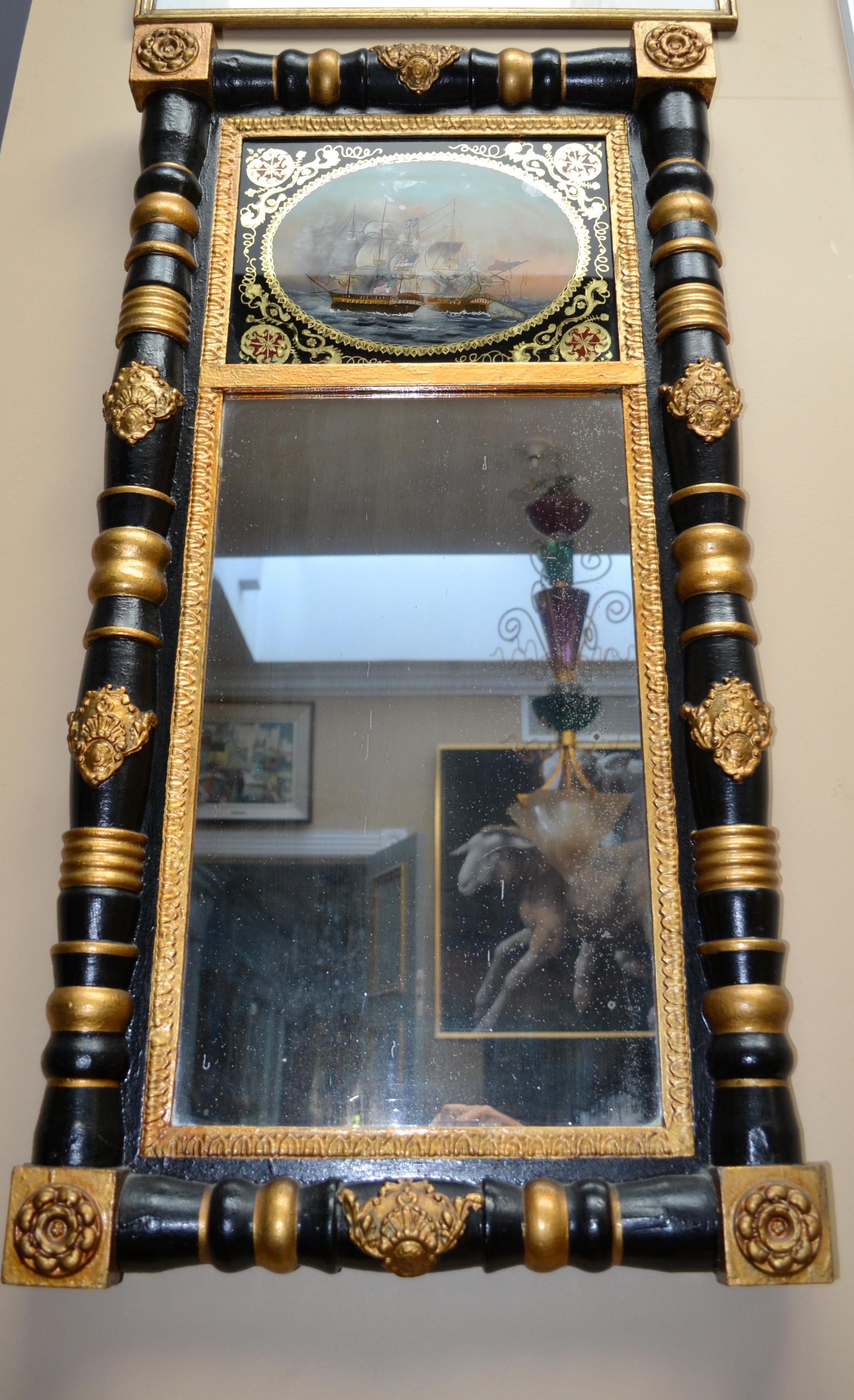 An American Federal Period mirror with an églomisé naval battle scene. The rectangular ebonized wood framed mirror is in two sections bordered with half turned columns decorated with gilding, the lower section is glazed, the top section shows an