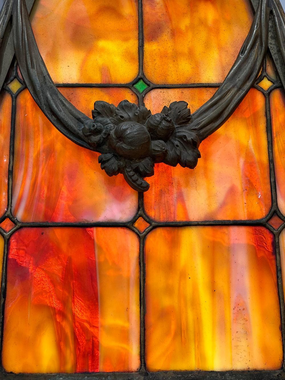 Un apparecchio da biliardo in vetro piombato e bronzo dorato dei primi del Novecento. Il paralume ha un vetro piombato di colore rosso, arancione e giallo, che nasconde 8 prese. La cornice con dettagli di nastri e festoni floreali. Circa 1900.