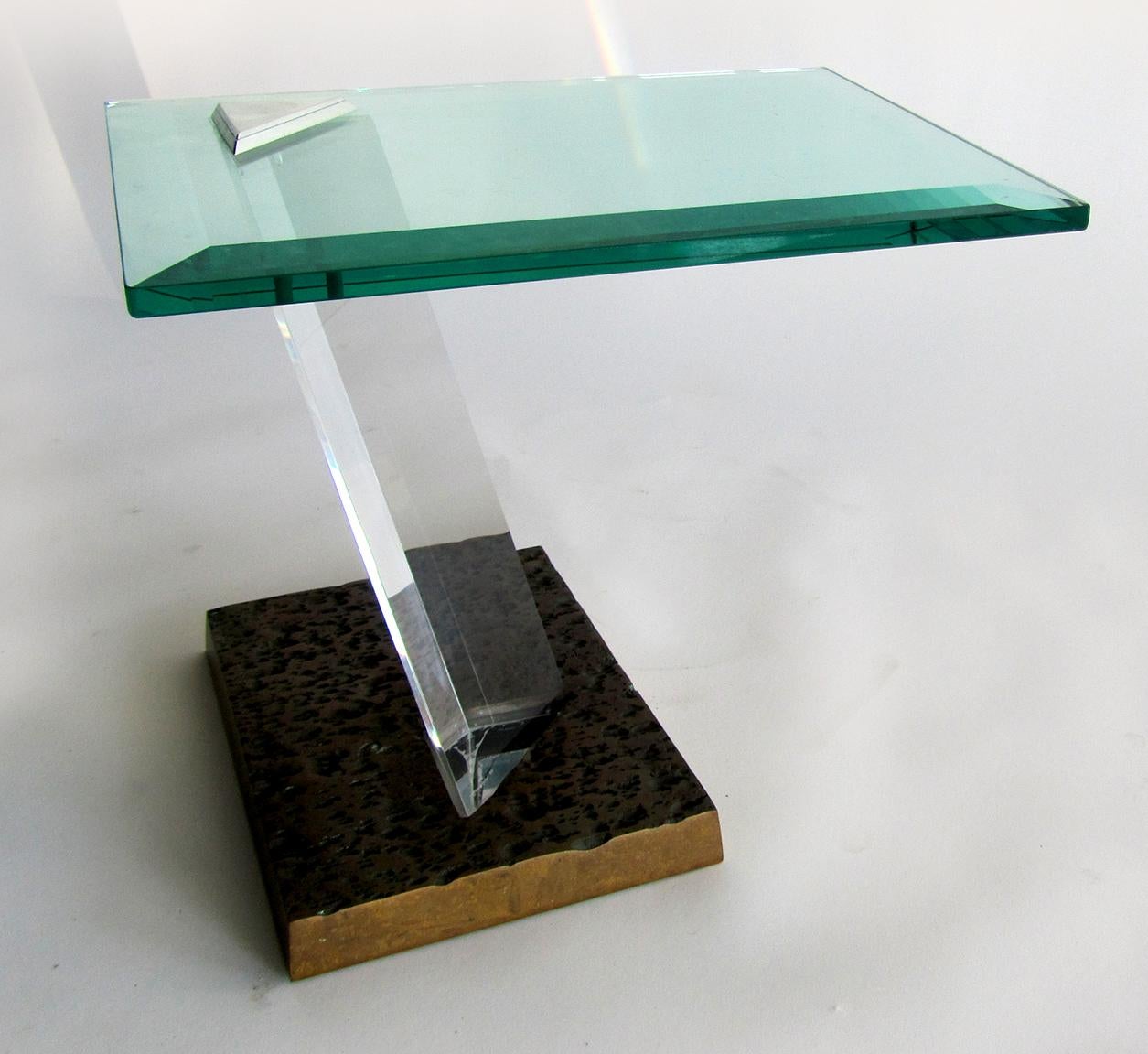 A sculptural side table by Jeffrey Bigelow, with a weighted bronze Brutalist base. The pedestal is faceted, angled Lucite and joins the base with the glass top. The Lucite is signed. The modern lines and weightlessness of this piece make this an