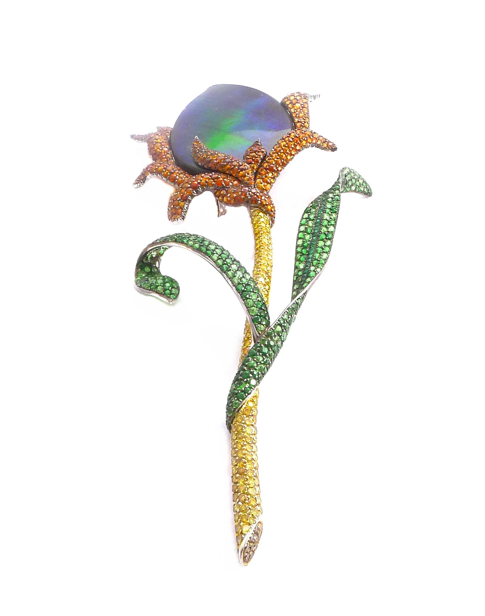Designed as a flower centering an ammolite (fossilzed opal) surrounded by tsavorites, green garnets leaves and yellow diamonds stem

Mounted in 18k yellow gold

- 1 Ammolite (fossilzed opal): 109.47 ct
- Tsavorites: 13.60 ct total
- Green garnets: