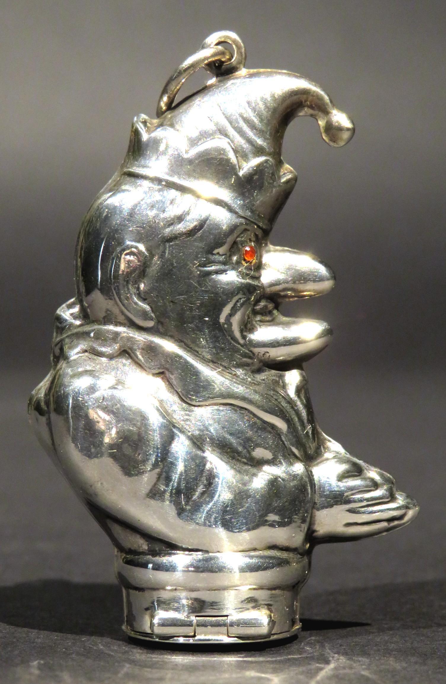 Un divertente porta vesta in argento sterling con le sembianze di Mr. Punch. La faccia è incisa con occhi di pietra rossa e dotata di un anello di sospensione, mentre la parte inferiore della base incernierata presenta una scanalatura dentellata,