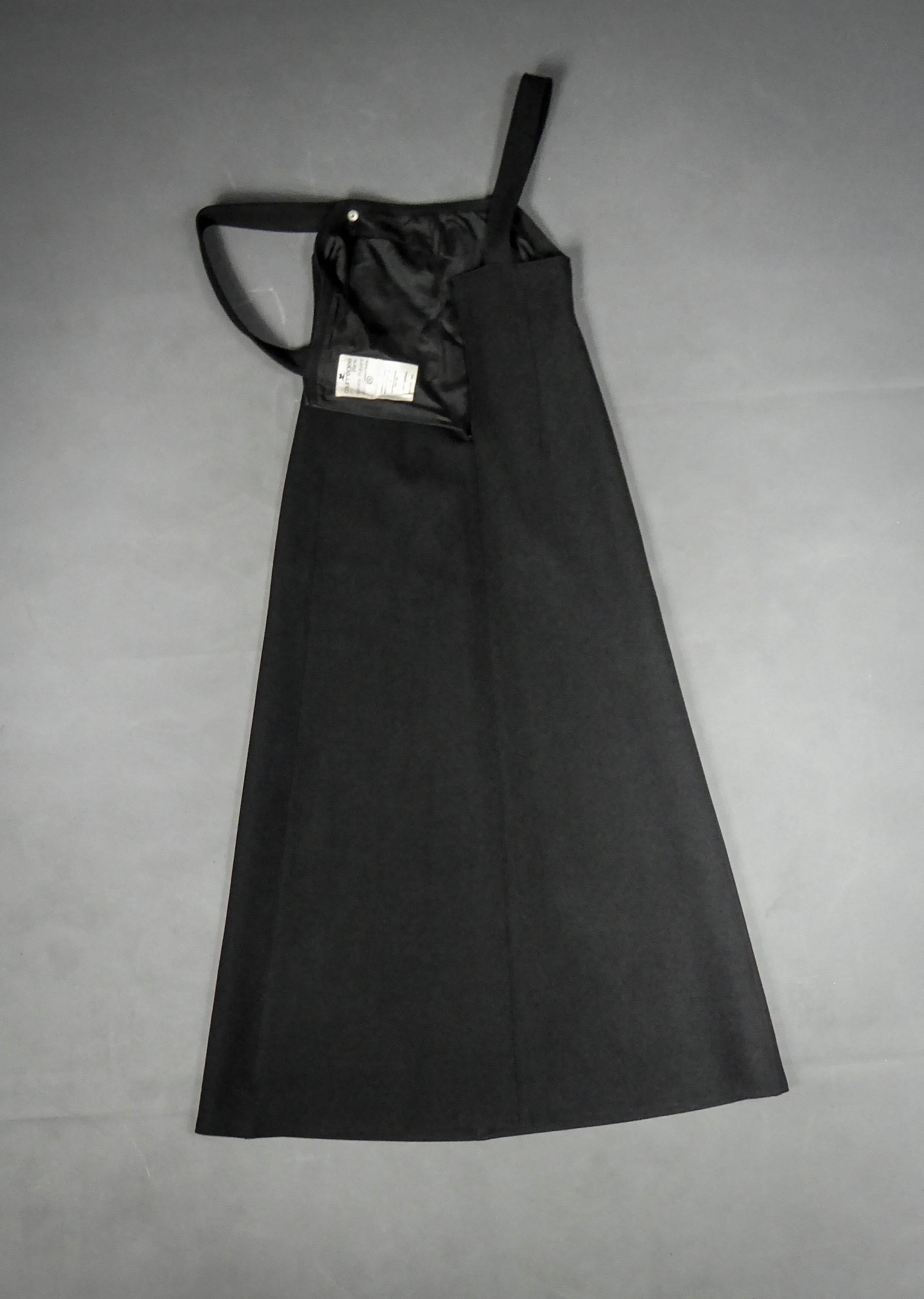 Circa 1970-1975 France
Robe tunique Chasuble inspirée du trapèze en jersey sergé de laine noire par André Courrèges. Sans manches et dos nu retenu par deux épaisses bretelles avec bouton pression laqué noir. Structure minimaliste composée de 4