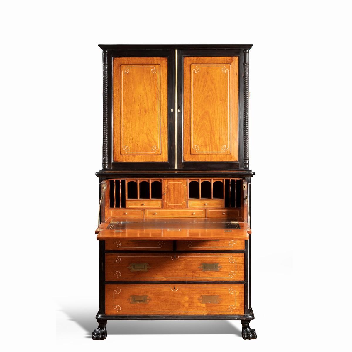 An Anglo-Chinese camphor and ebony campaign secretaire bookcase, of rectangular form in two sections, each with carrying handles, the upper section with cupboard doors which open to reveal two adjustable shelves, the lower section with a secretaire