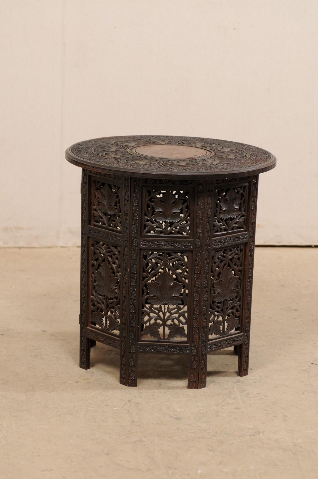 An Anglo-Indian hand carved side table with round top from the mid-20th century. This vintage table from India, with a round-shaped top measuring approximately 21
