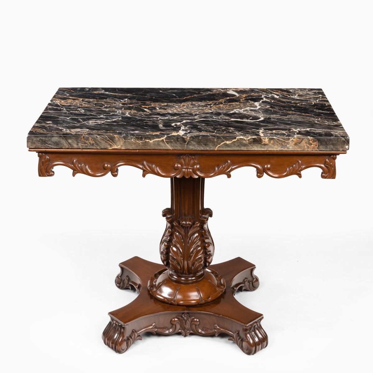 An Anglo-Indian mahogany table with Nero portoro marble top by White and Co Calcutta, the rectangular marble top set on a shaped frieze carved with leafy scrolls the reeded column support emerging from four fleshy acanthus leaves, all on an X-shaped