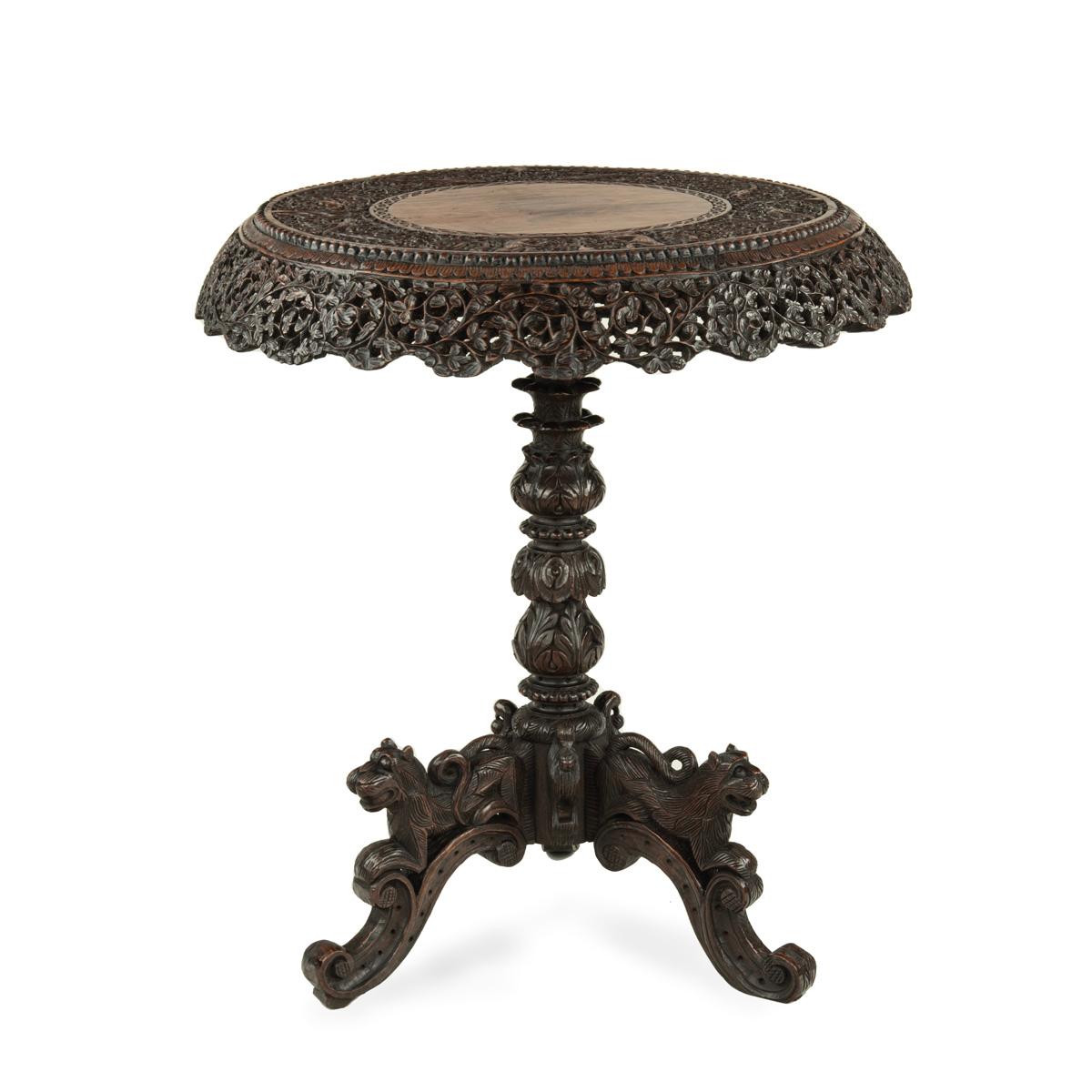 An Anglo Indian padouk tripod side table, of circular form, the top with a solid centre within a border and curved frieze of openwork filigree foliage enclosing paired stylised monkeys and birds, the support with tiers of palm fronds raised on three