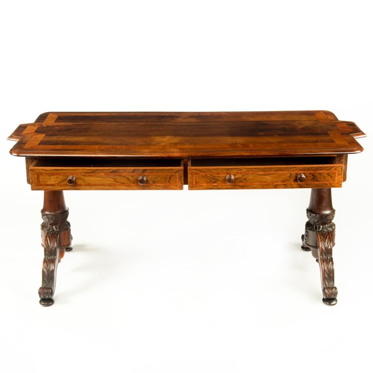 An Anglo Indian rosewood end support library table, the rectangular top with shaped short sides, decorated with wide satinwood banding, the frieze with two drawers on one side and two dummy drawers on the reverse all with herringbone veneers and