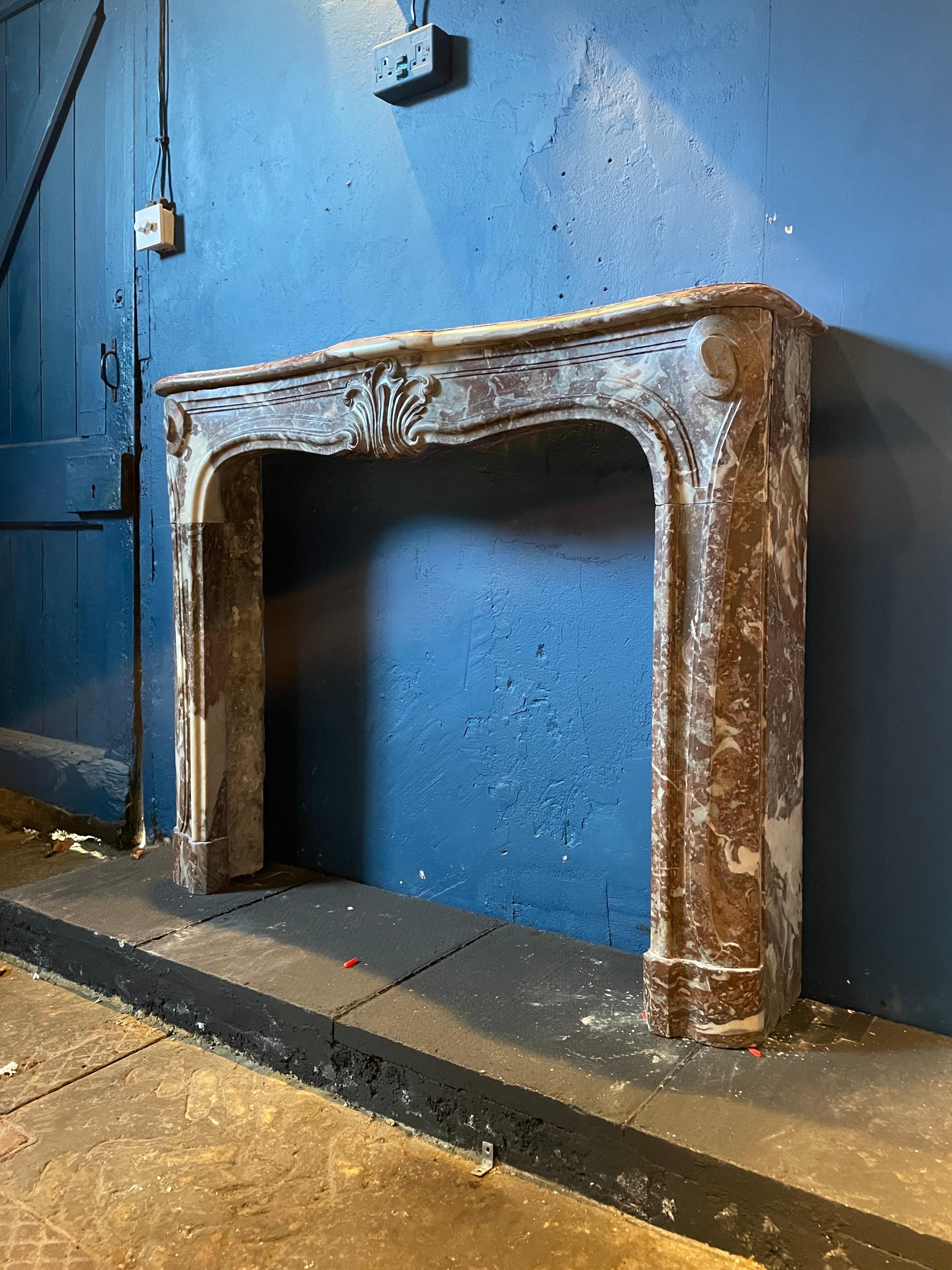 A transitional marble fireplace from the late 18th century in northern regional variegated red marble. Compact in size yet well carved with central feather cartouche flanked by sweeping carved jams surmounted with C scrolls.  A deeply shaped