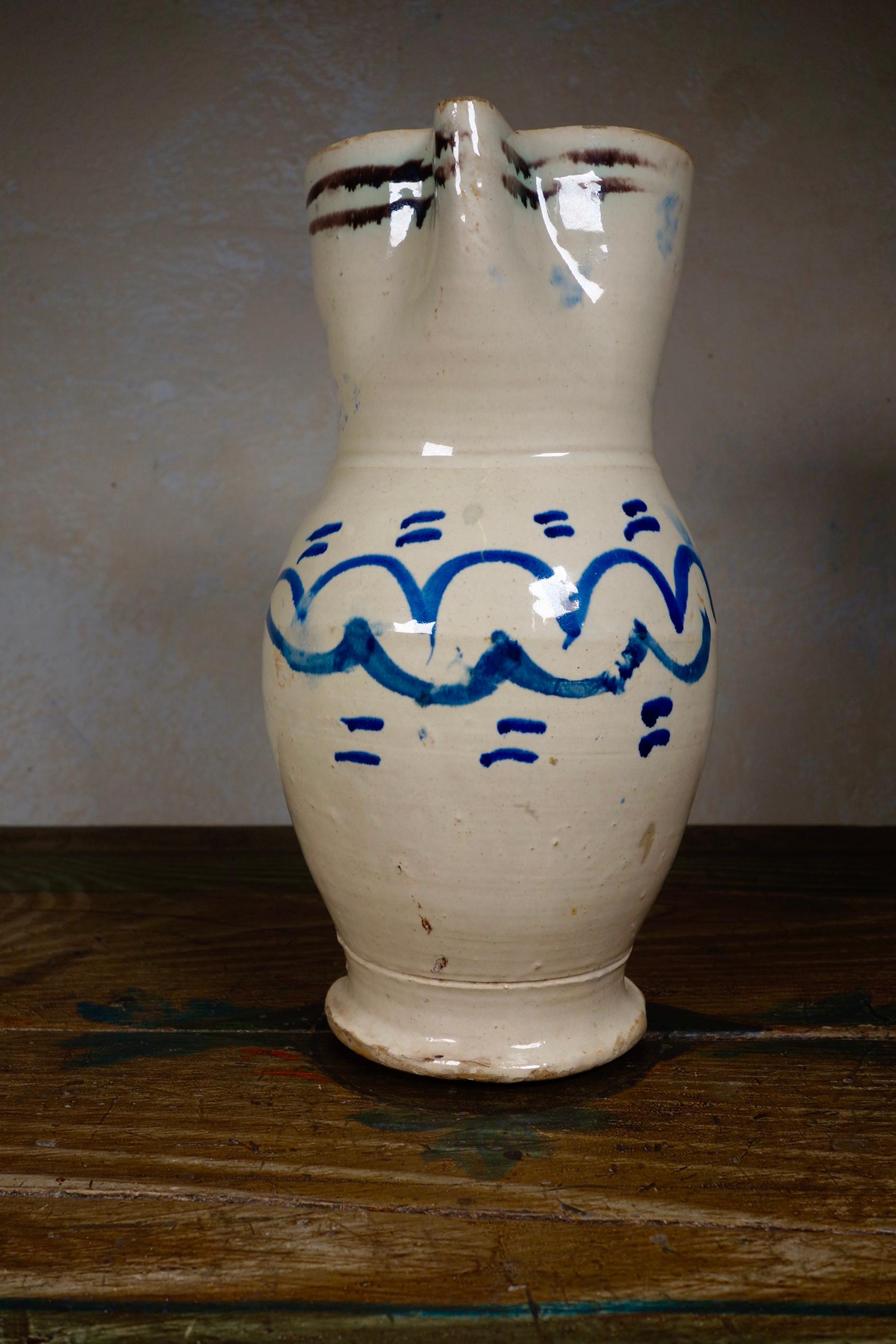A large antique tin-glaze Pugliese Pitcher. 
Featuring an elongated ovoid-shape body with a disc foot. The flat strap handle rises from just under the rim and ends just before the widest part of the lower body. 
Painted with simple geometric