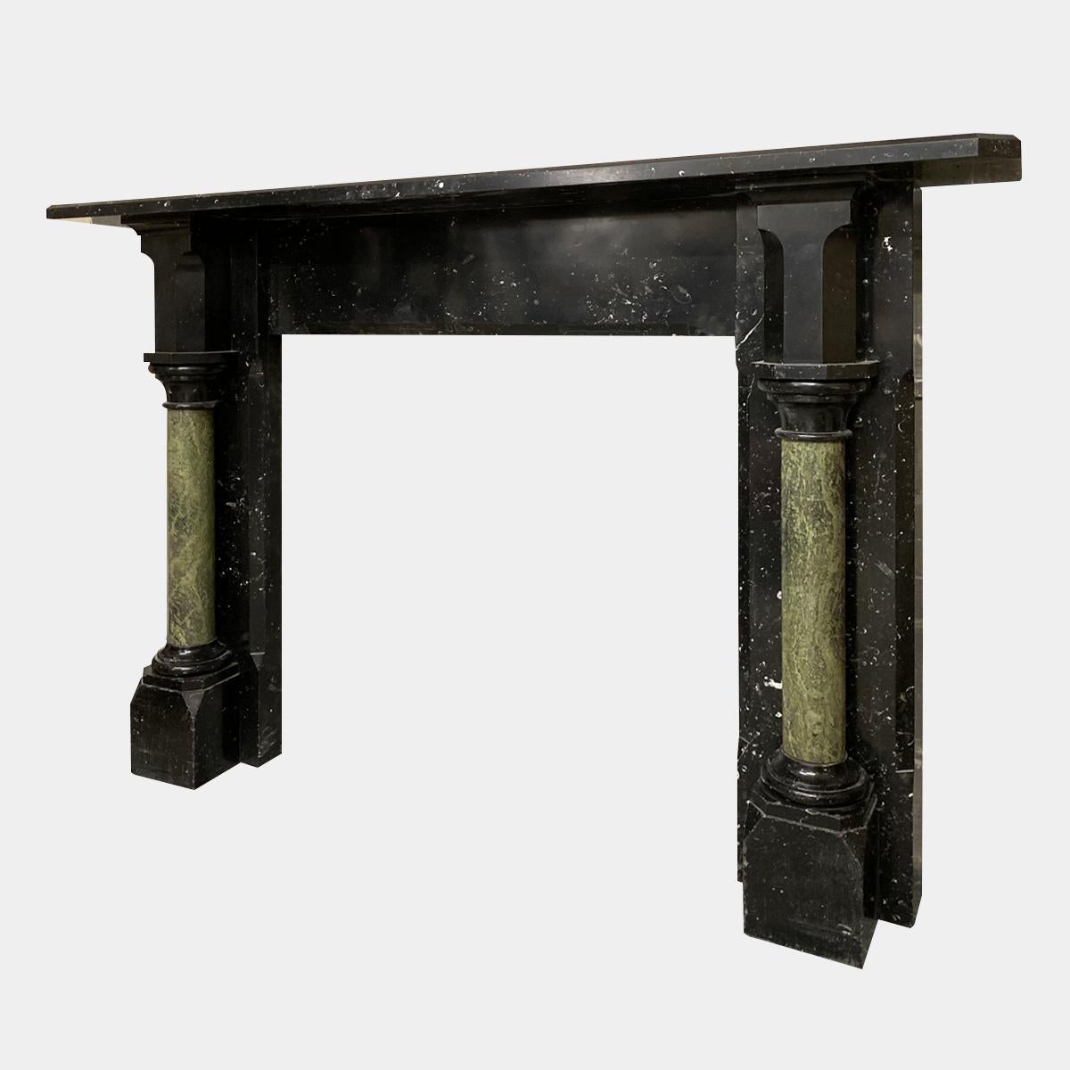 A large and imposing Gothic Revival fireplace in Irish black Kilkenny fossil marble with green Connemara marble columns. A plain frieze with simple tapered moulding, flanked by semi hexagonal corner blocks which are supported by fully disengaged