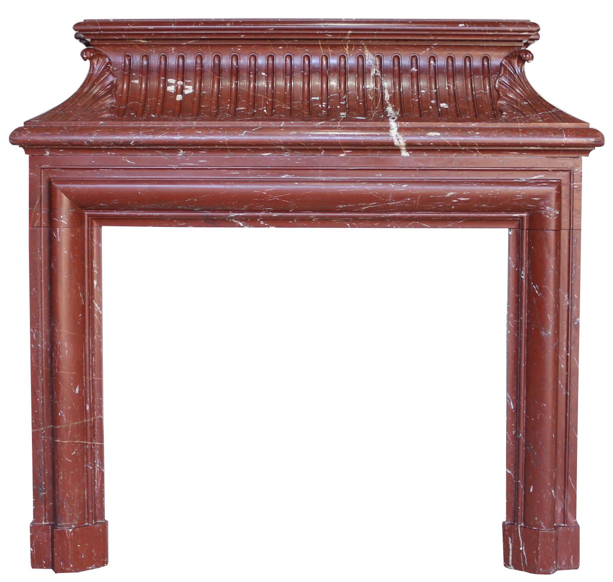A tall, Louis XIV ‘Bolection de Versailles’ antique chimney-piece or fire place in richly coloured cherry red Griotte marble. The concave fluted frieze with scaled corner foliage decoration. The side pieces feature decorative circular hinged brass