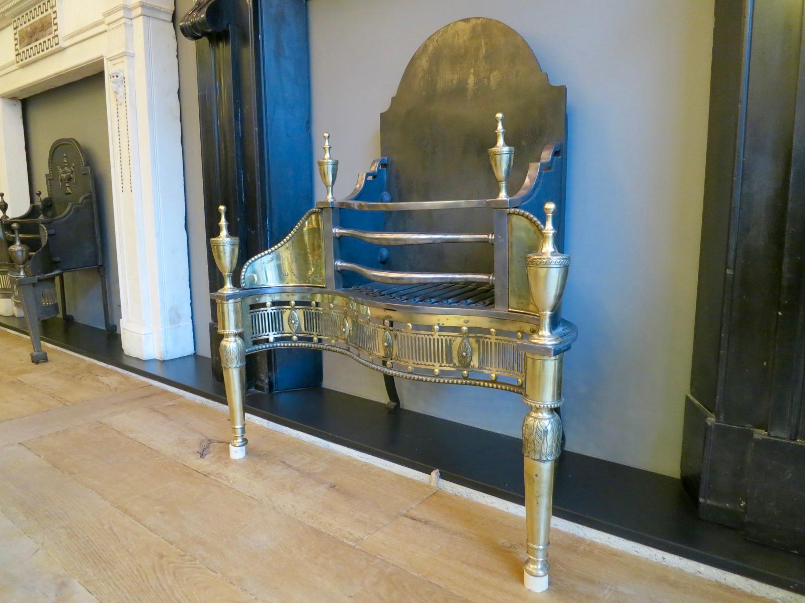 A 19th century fire grate with tapering front supports with acanthus detail and surmounted by classical urn finials. The wings engraved with tied ribbons, bell drops and oval patarae, flanking a bowed bar burning area, above a serpentine pierced