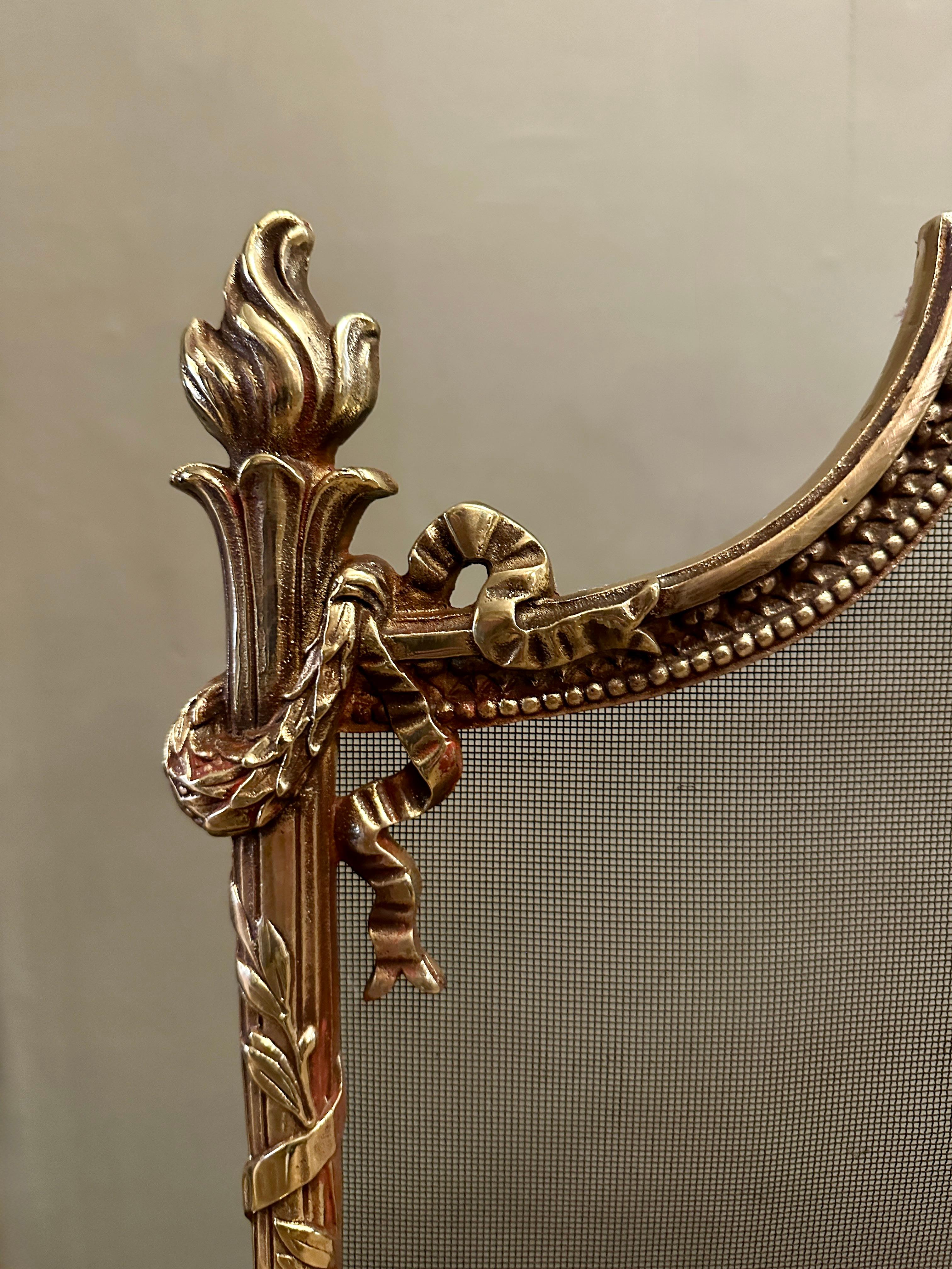 Antico parafuoco inglese della fine del XIX secolo, con montanti a forma di torcia, fiocco legato e decorazione a foglie di alloro. Il grembiule con le volute e i piedi larghi e strombati. Rete antincendio nera dietro 

Inglese Circa 1890-1900