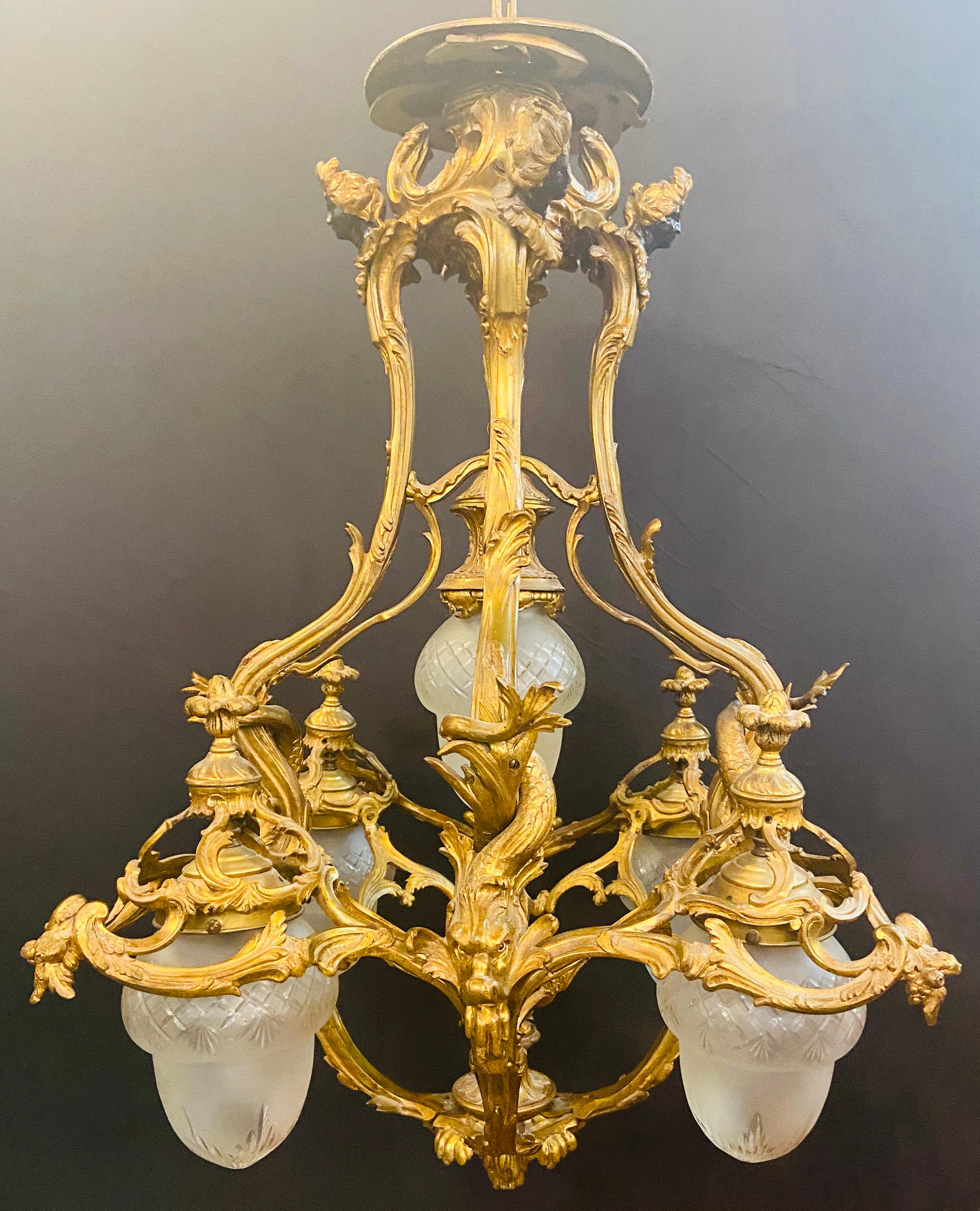A spectacular 19th century French Louis XVI chandelier having 5-light. Featuring it is original Rene Lalique style white milk shades and a fine bronze carving style, the chandelier collar is decorated with four women heads looking forward and giving