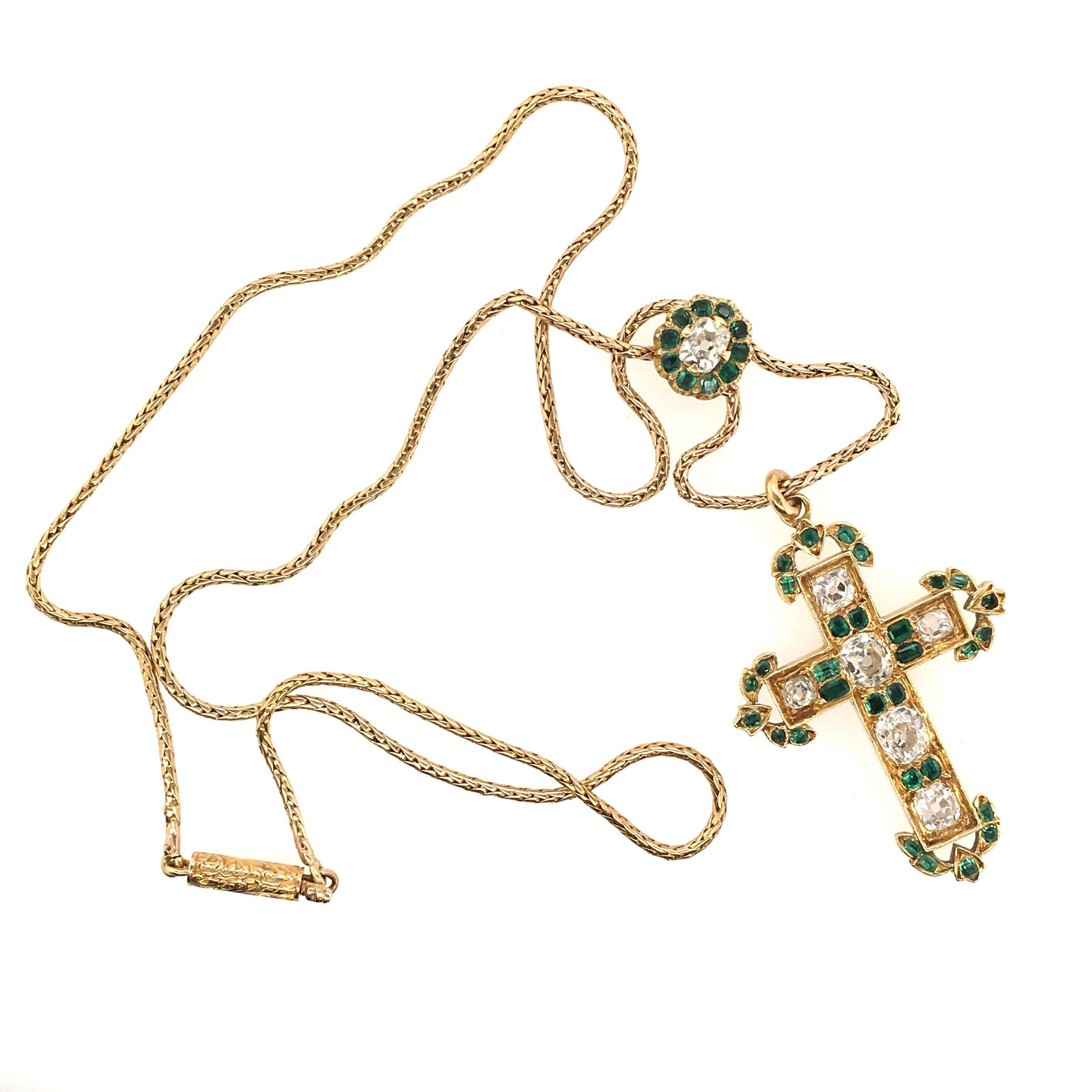 An antique 18 karat yellow gold, diamond and emerald cross pendant necklace. Circa 1890. Set with old mine cut diamonds, enhanced by old cut emerald foliate motifs, suspended from a fine spiga chain enhanced by an old cut diamond and emerald floret