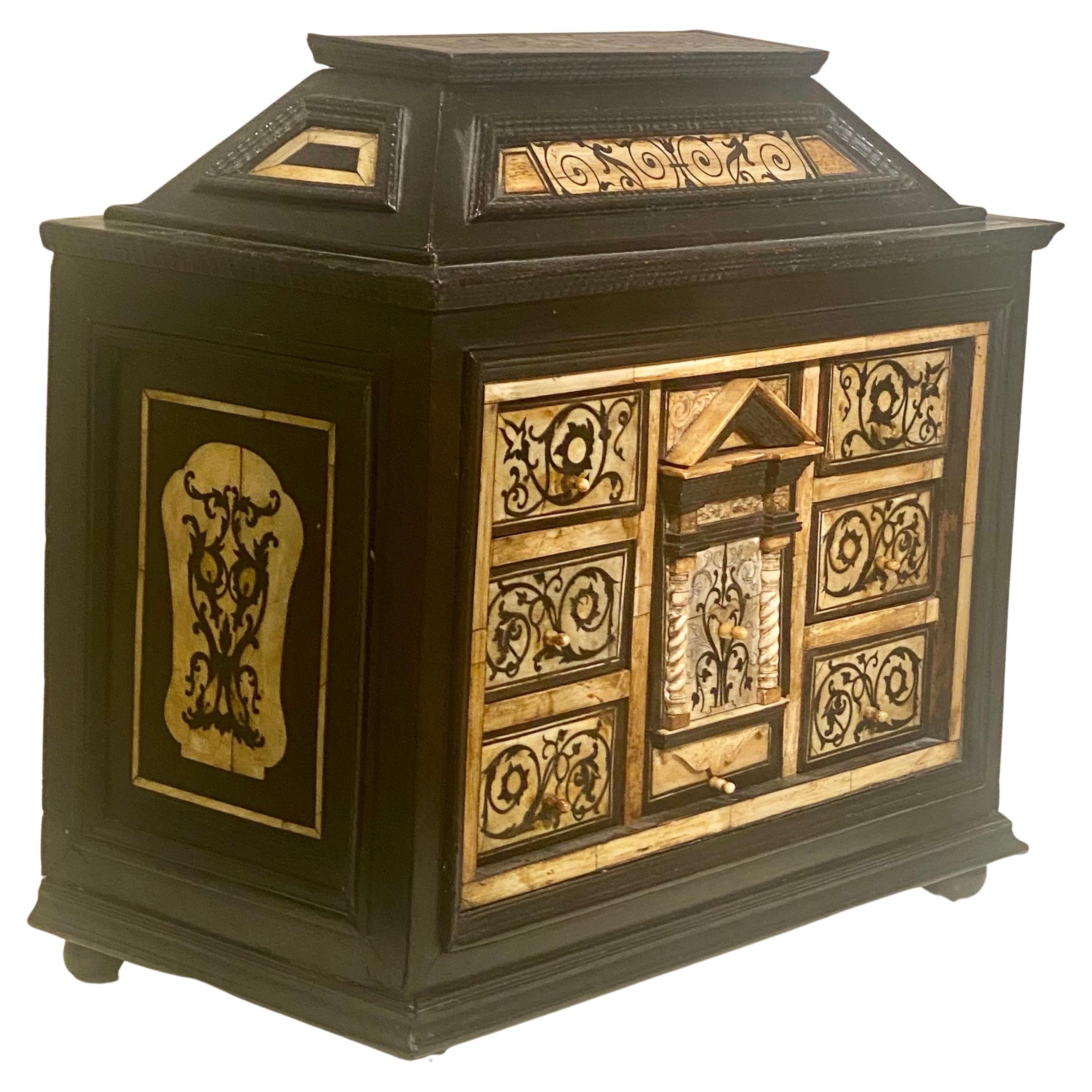 This precious table cabinet opens with a lid and has nine drawers richly decorated with ivory and ebony marquetry depicting foliage and scrolls, each drawer has an ivory pull button. The top of the lid has a similar design of ivory foliage on ebony