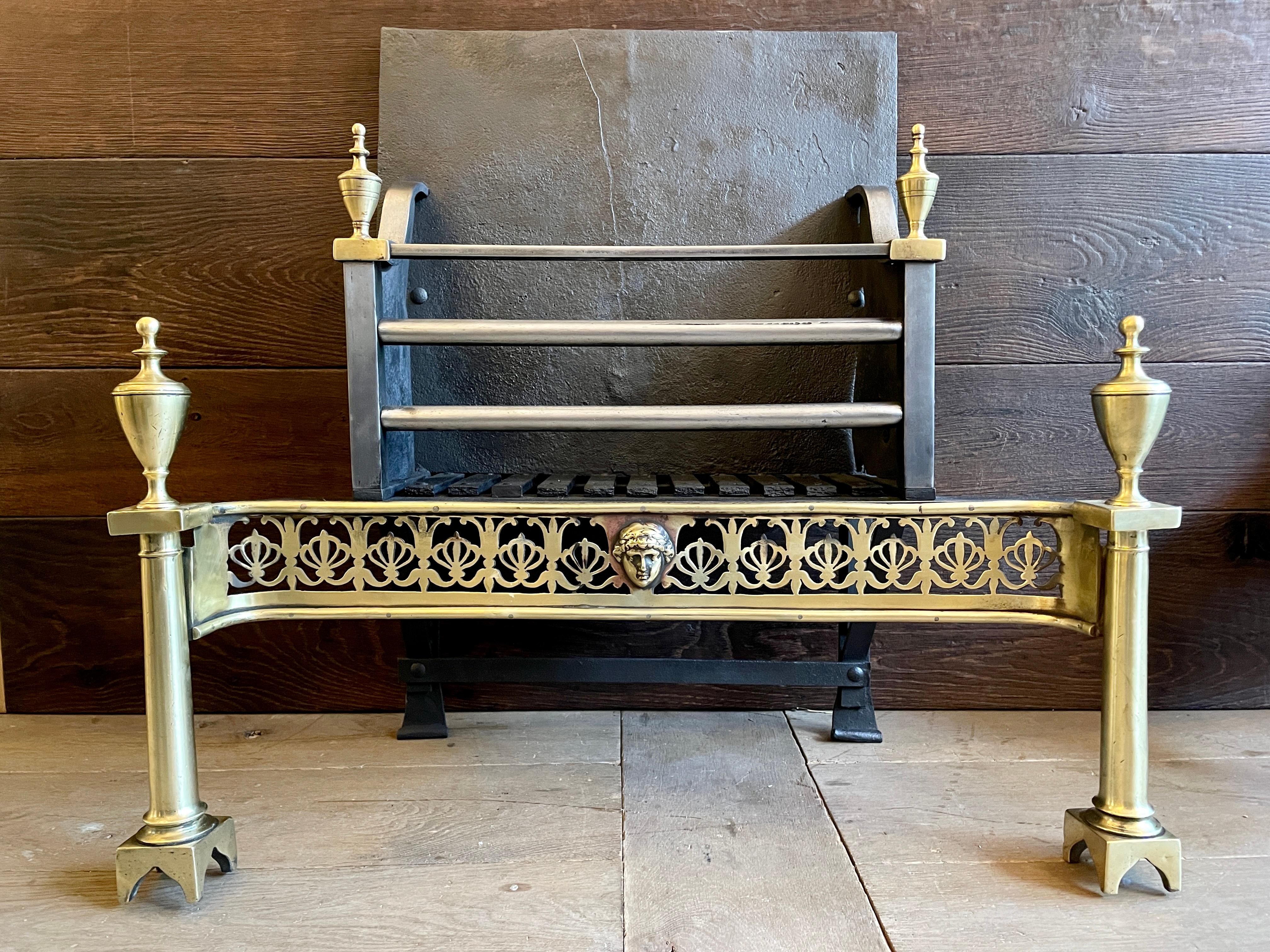 A Brass and steel fire grate with wrought iron back feet and cast iron fire back. The column front supports with domed cut feet and surmounted by large finials all in brass flanking and intricately cut and pierced fret with male cameo to centre. The