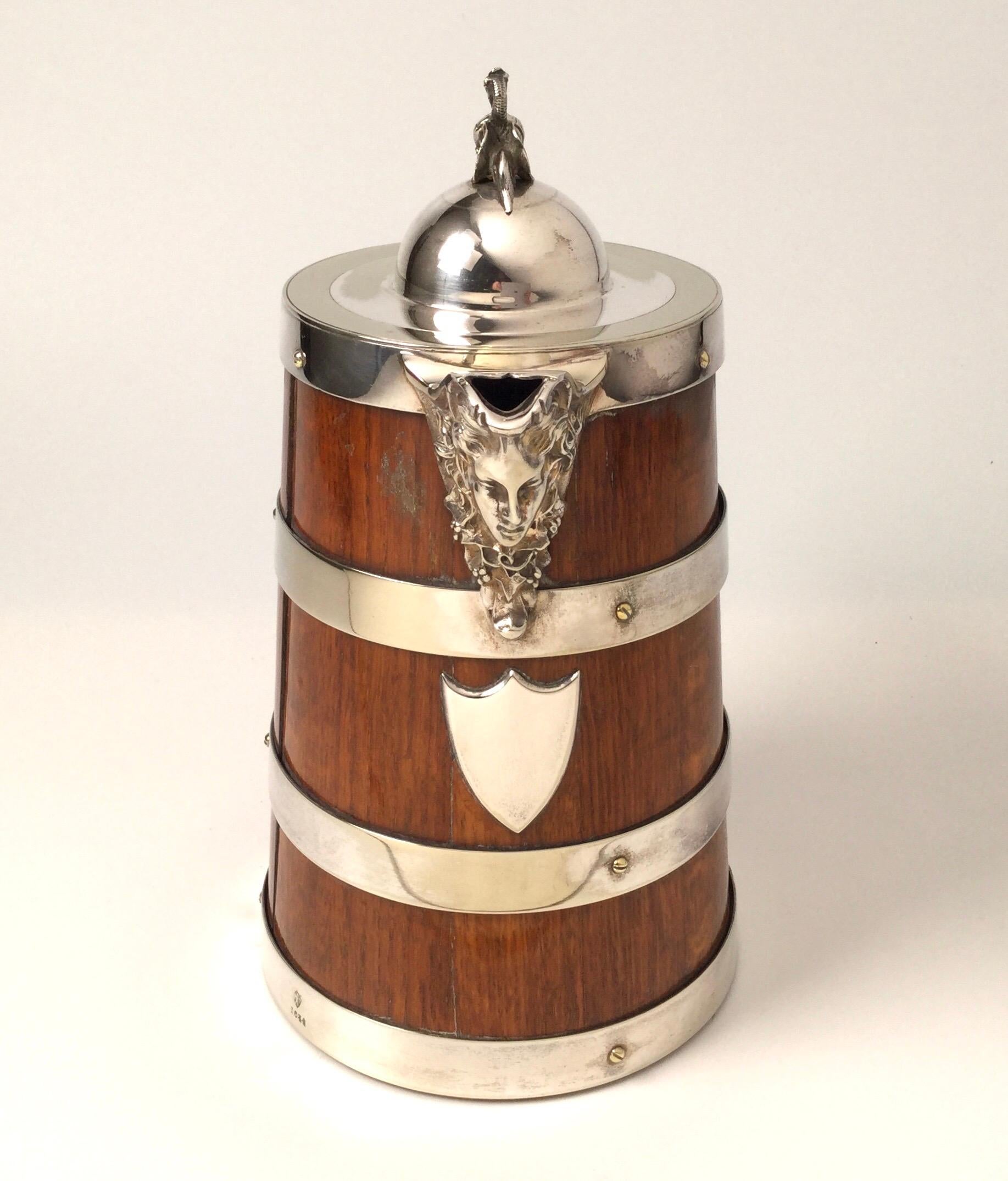Handsome 19th century Tankard in oak with silver plated bands. The makers mark is John Grinsel & Sons. The handle with a detailed female ships figure and the spout with a figural mask. We also have a larger on that is also posted. This tankard is 10
