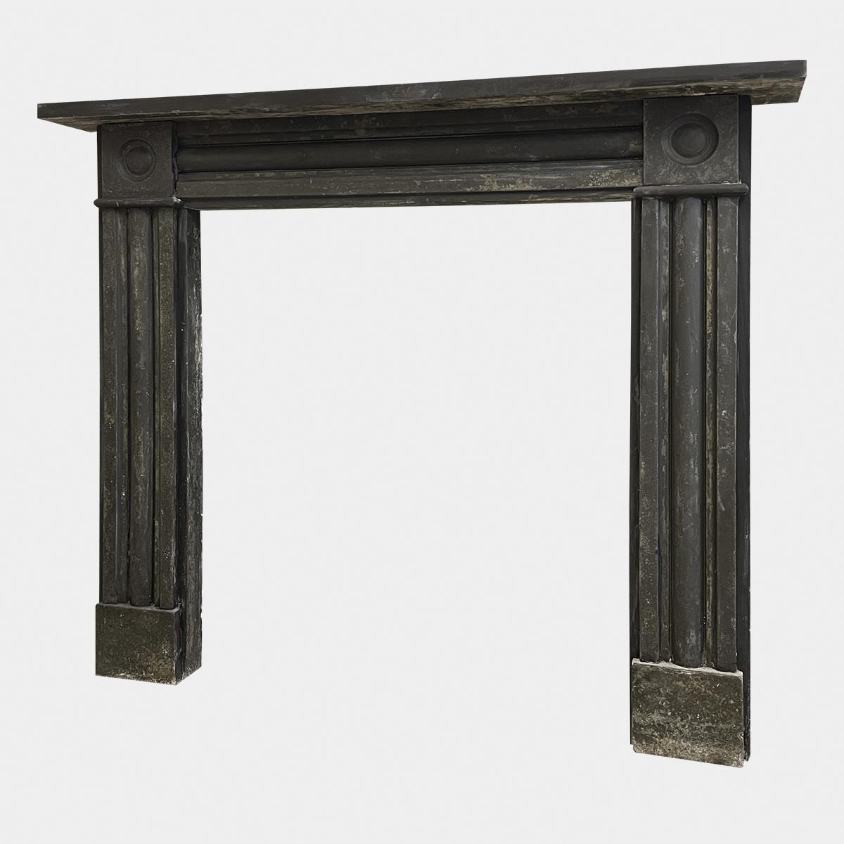 An English Regency period Slate fireplace from the early 19th century, circa 1815. 
The cushion panelled jambs on square foot blocks terminating in carved roundel corner blocks. The conforming frieze again in a cushion moulding with simple shelf