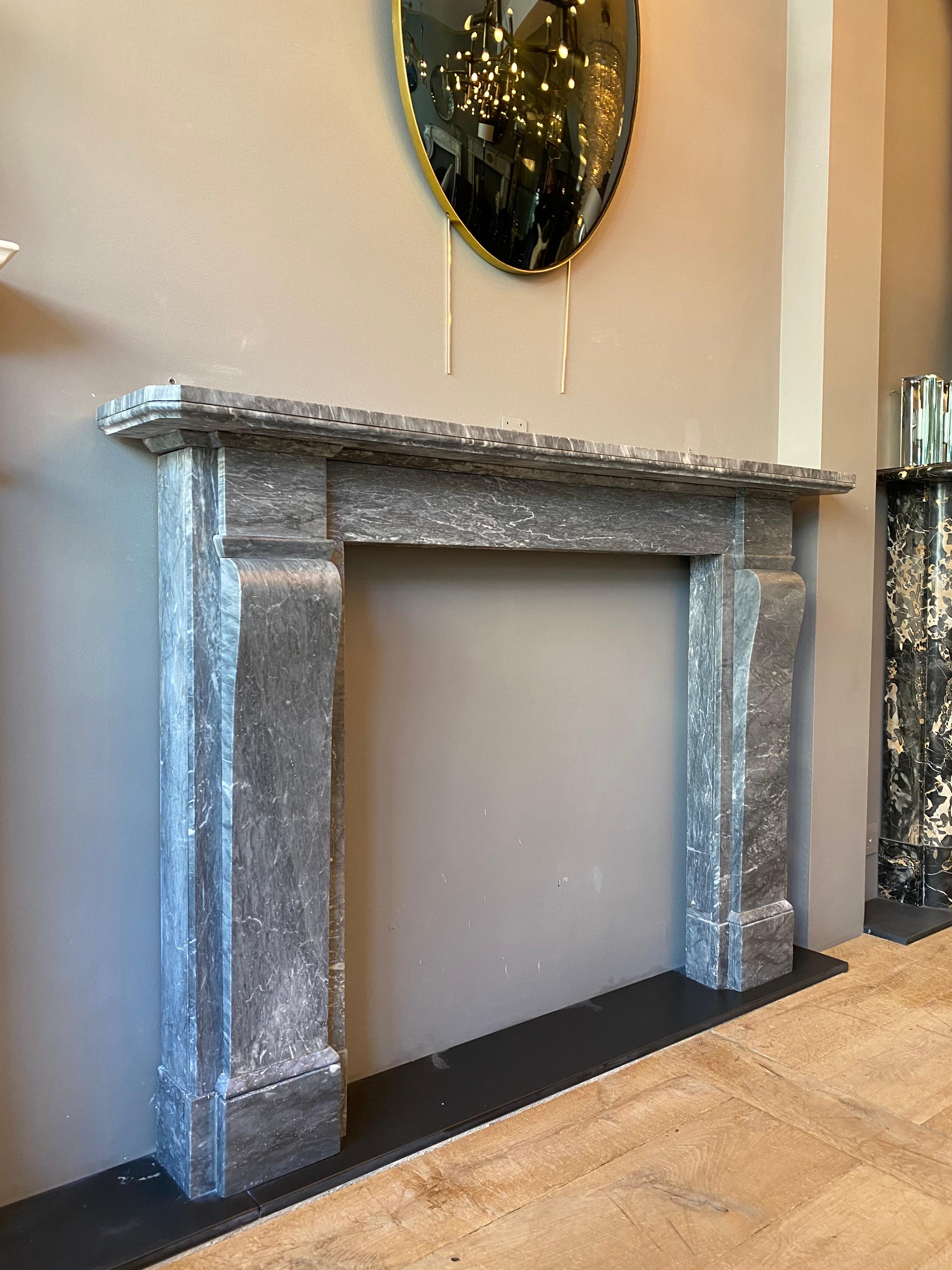 An English Regency early 19th century surround in Italian Bardiglio marble. The console jambs surmounted by plain corner blocks and supported on separate foot blocks. The slim high frieze with a shaped under mantel (fireplace) moulding, beneath a