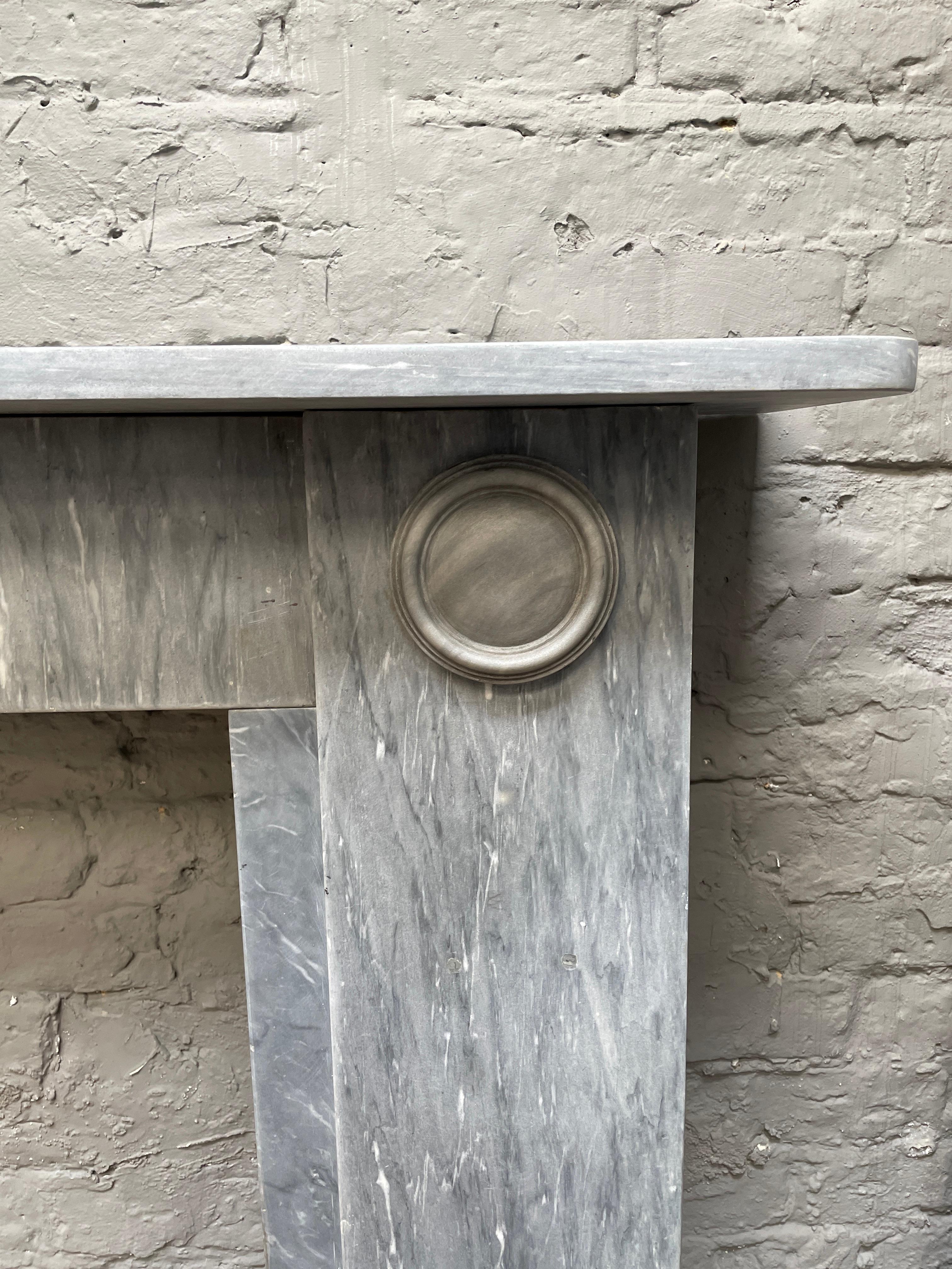 An elegant and rare model of a Regency period fireplace, in Dove Grey Italian Bardiglio marble. Its simple architectural lines, very much in the manner of Sir John Soane. The slim plain frieze, between two simple, pilaster jambs with carved roundel