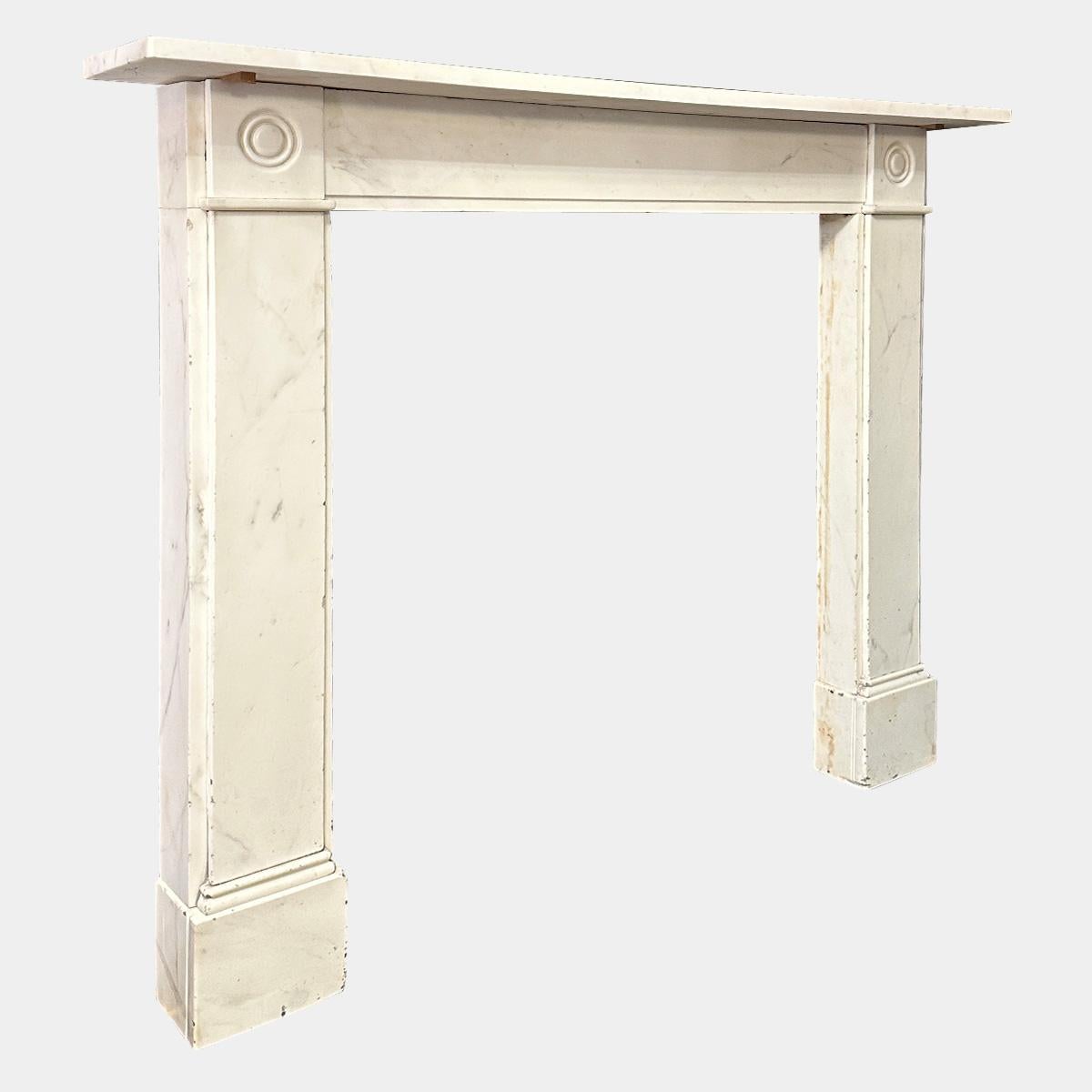 A very late 18th or turn of the 19th century English fireplace In Italian Statuary white marble. The plain pilaster jambs stood on separate foot blocks, surmounted by carved roundel corner blocks. A simple stepped frieze between matching the width