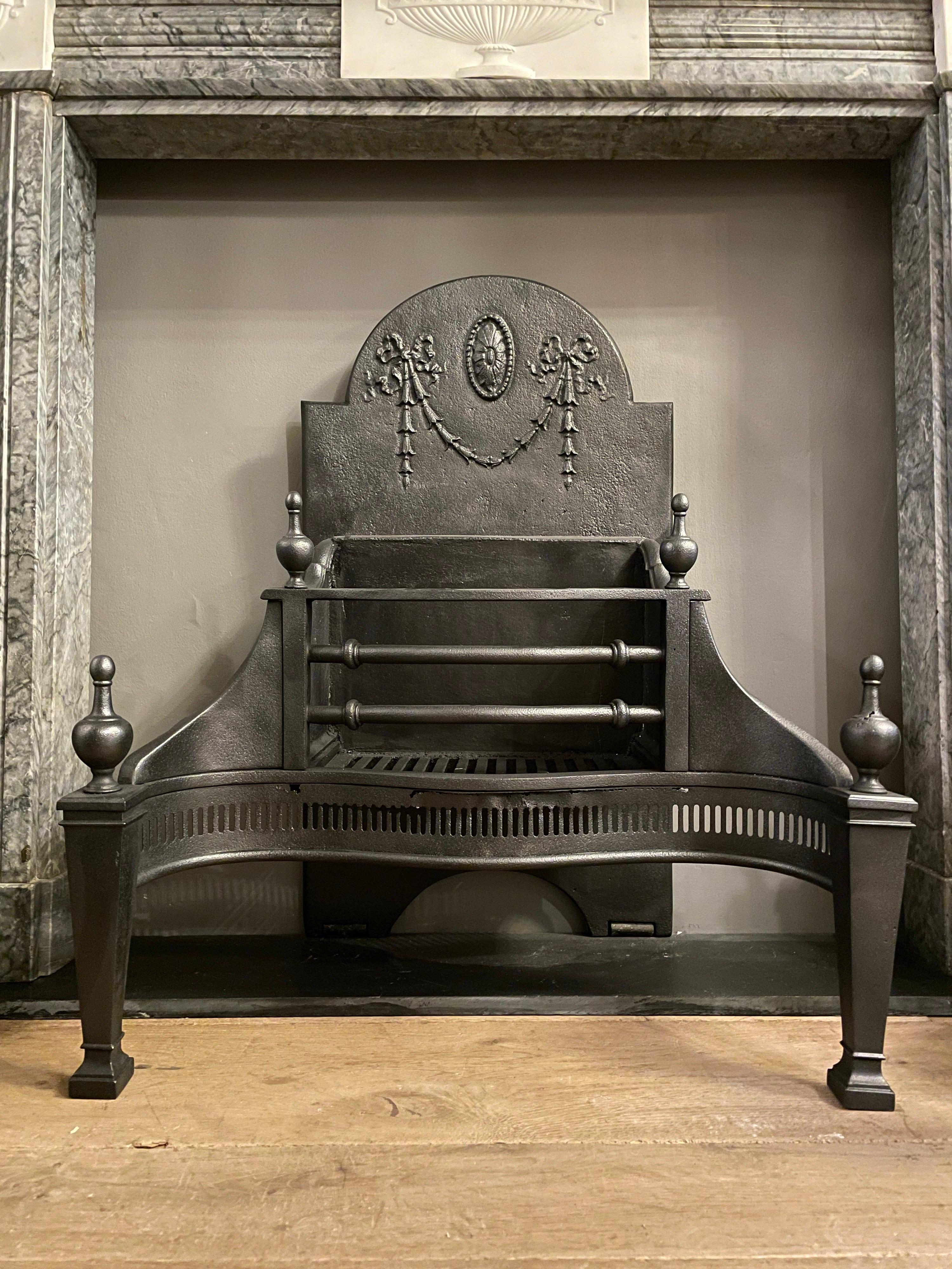 A lead polished steel fire grate in the Georgian manner, with tapering columned legs caped with finials. Plain wings with decorative burning bars and a fireback with oval patarae and bell drop drapery and wheels for movement at base. The fluted fret