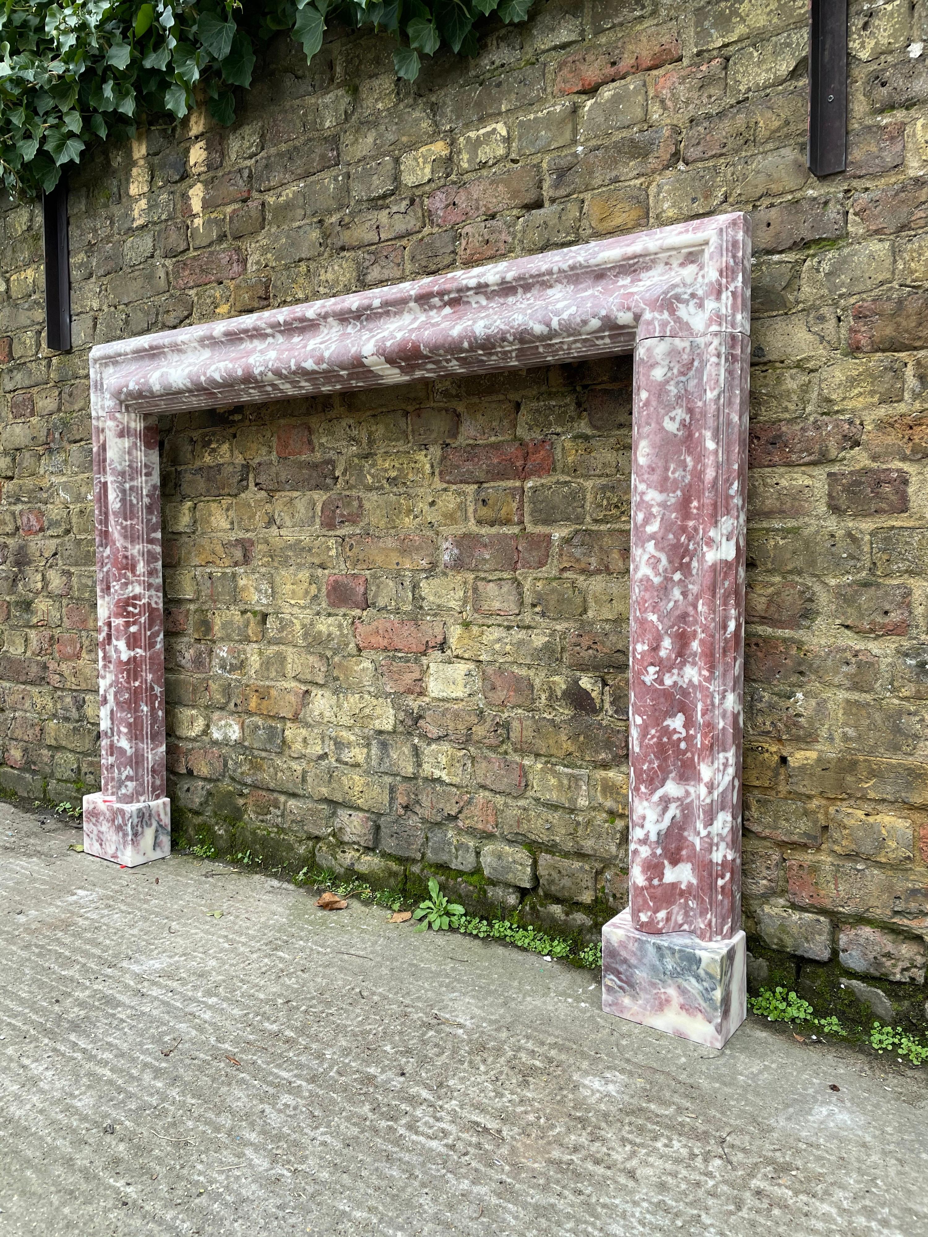An antique 19th century English Bolection moulded fireplace in Fleur De Peche marble. The moulded frame supported on square foot blocks. An elegant piece executed in a rare and superior marble.

Opening sizes 97cm H x 113.5 W.