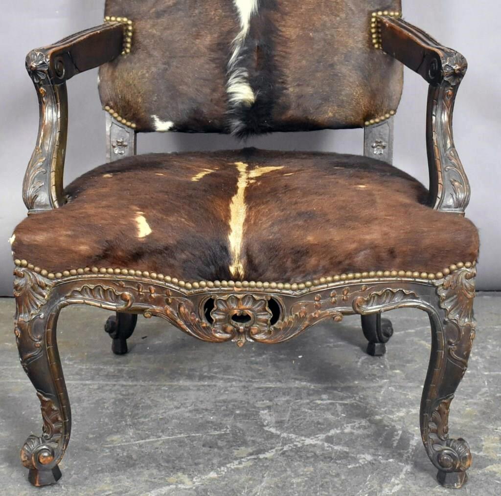 An antique French armchair from France. A hand carved solid wood frame and brass detailing in good condition. Upholstered in cowhide beautifully centered. Wear consistent with age and use, circa late 19th century, France.