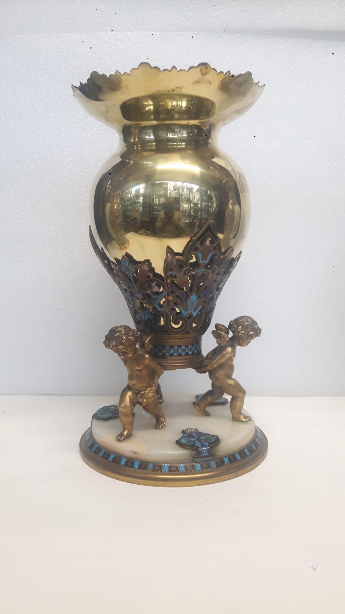 An antique French champlevé enamelled vase with a polished gilt metal body upheld by two putti in gilt bronze on a white marble base,  the border decorated with a turquoise champlevé enamel design. The shapely gadrooned top part of the vase adds a