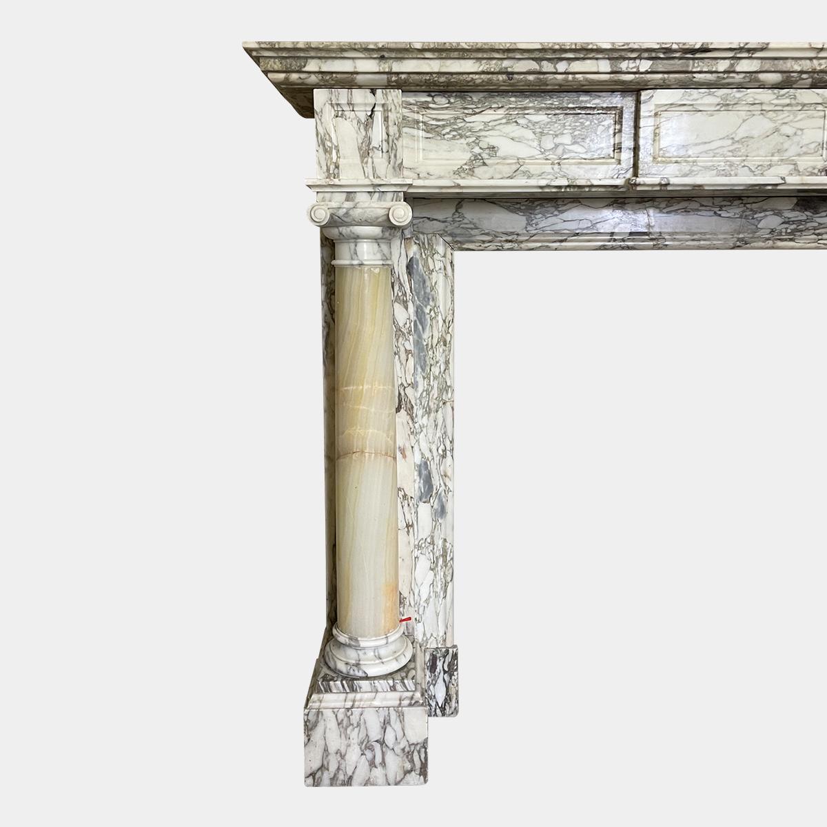 A large antique French fireplace in the neoclassical manner. Executed in quality Breche Marble. The jambs with Alabaster columns, supported on large square foot blocks with Ionic  capitals, surmounted by square fielded corner blocks. The panelled