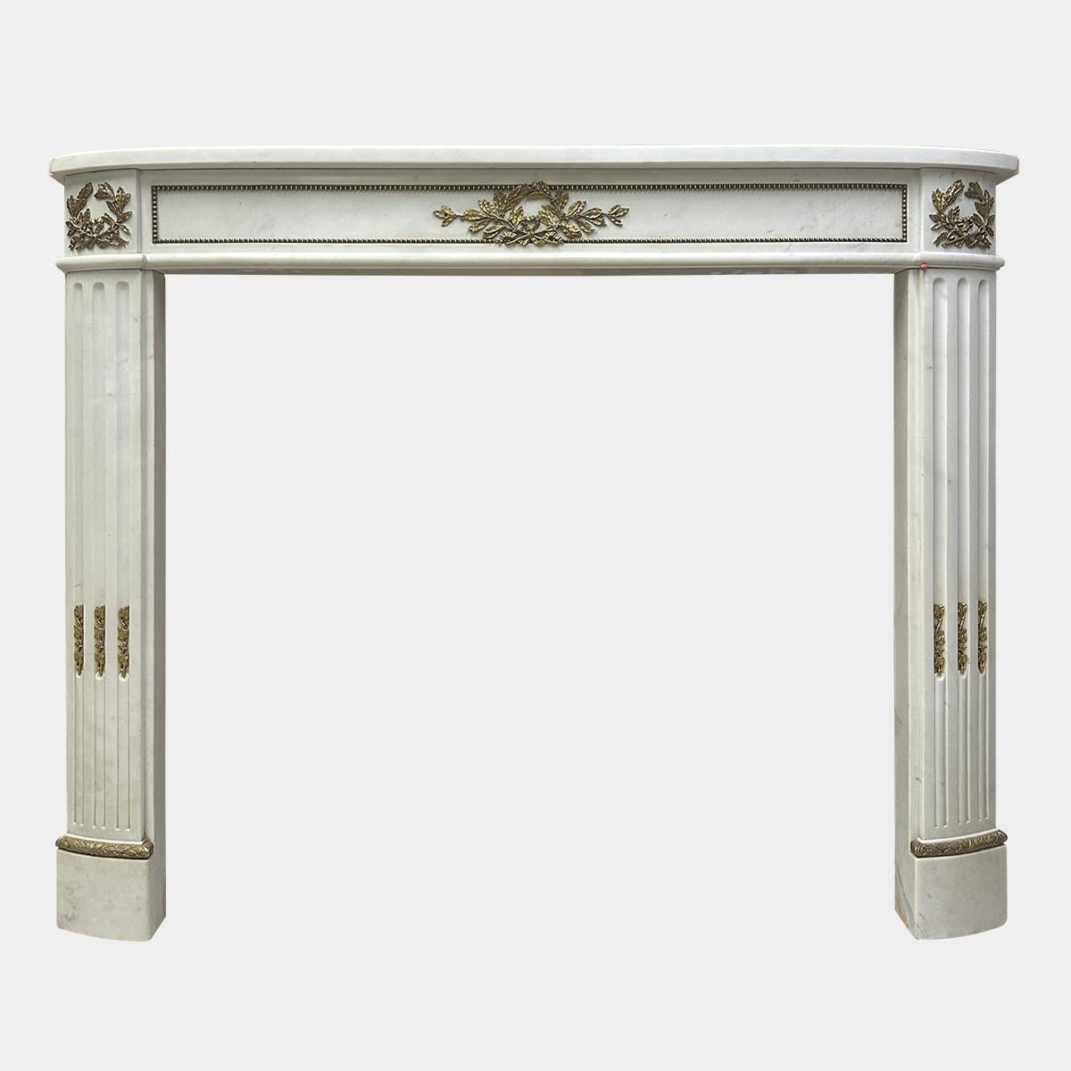 Una chimenea estatuaria de mármol blanco con montura de ormolu de principios del siglo XIX, de la época Imperio. Mármol y ormolina de gran calidad, con estante, friso y jambas en forma de demi lune. Friso con panel de cuentas de ormolina, adorno de