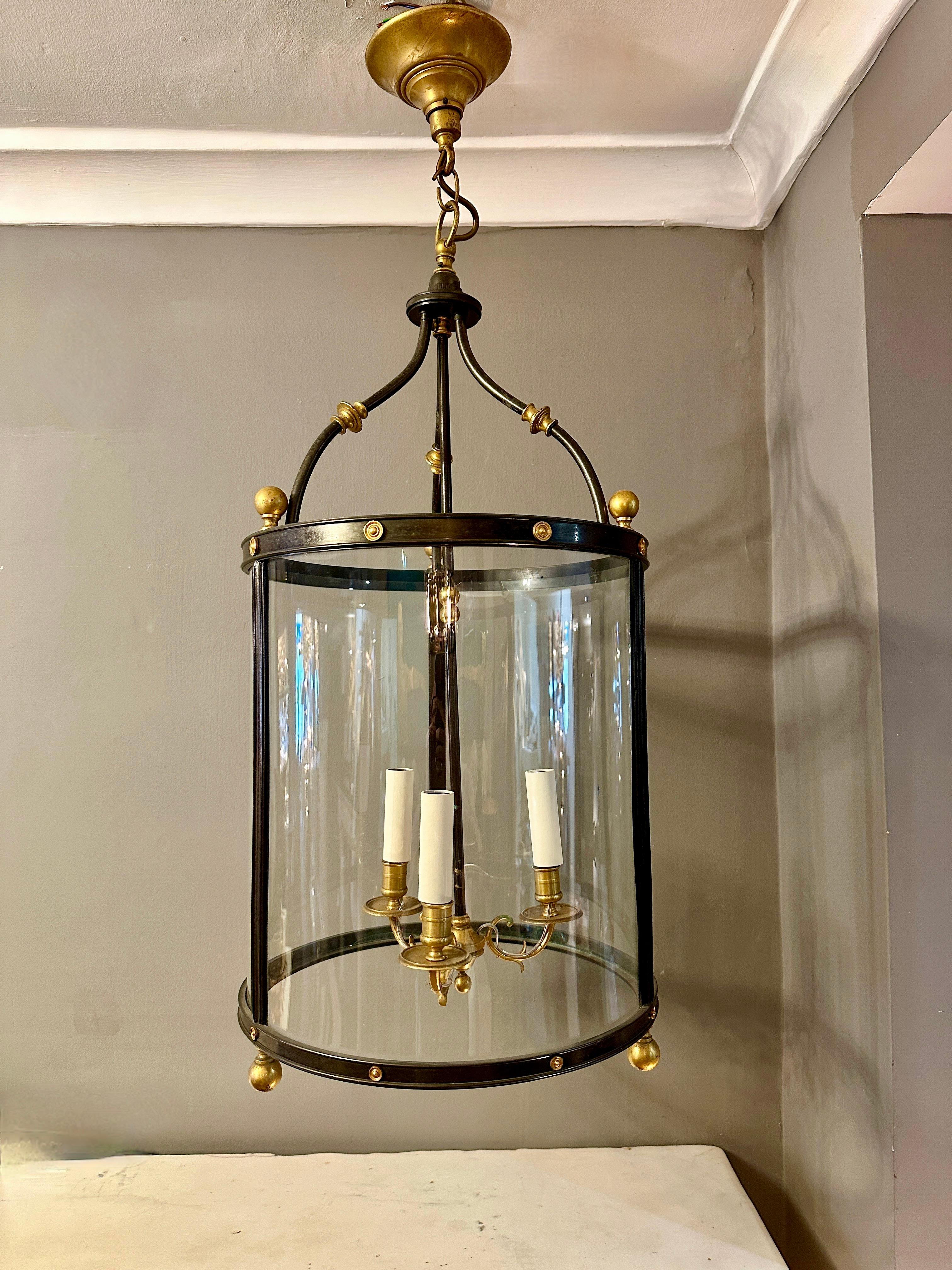 Une grande lanterne de style Empire en bronze patiné avec des accents en laiton doré. Quatre panneaux de verre incurvés, branches intérieures décoratives à volutes. Plafonnier en laiton doré. Re câblé. Fin du 19ème siècle ou peut-être plus tôt. 