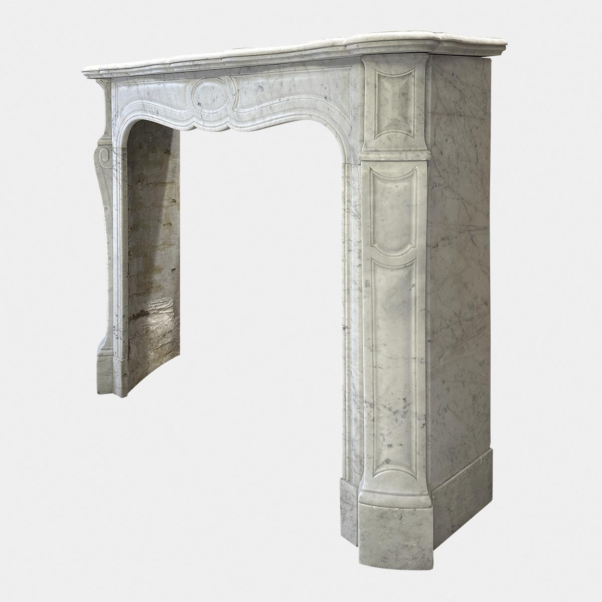 An antique late 19th c Carrara marble Louis XV Pompadour style fireplace. The serpentine shelf with mouldings underneath above a conforming serpentine frieze with oval panel to centre. Console cantered jambs with paneled corner blocks. Stood on