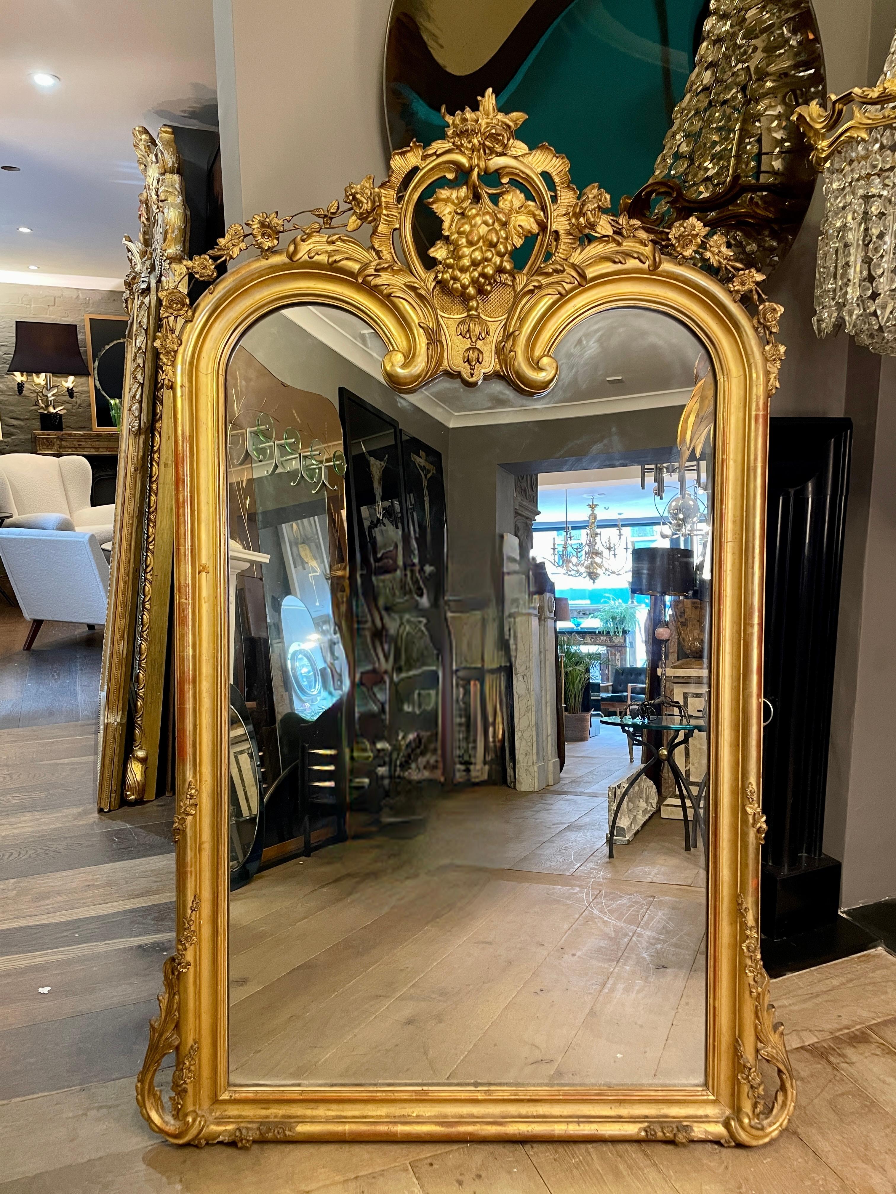 A very good quality early 19th century French gilt mirror in the Louis XV manner. Unusually shaped scrolled top to mirror plate under the elaborate large central cartouche of scrolled foliate with a large grapevine centre. Cascading from each side
