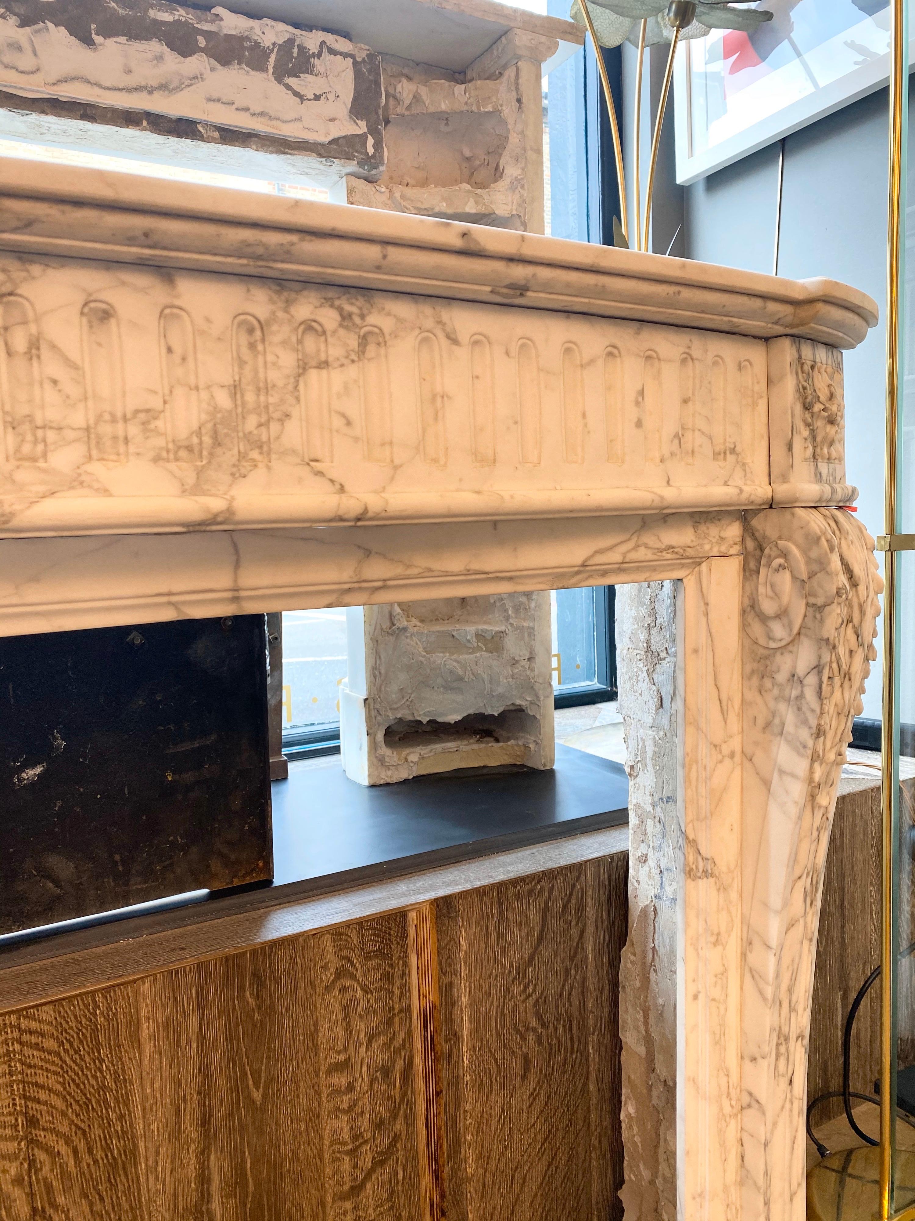 A well-proportioned Louis XVI style antique mid-19th century French fireplace in quality Calacatta marble. The bowed and stop fluted frieze beneath a bowed brake front shelf. The jambs adorned with carved acanthus and surmounted by square patarae